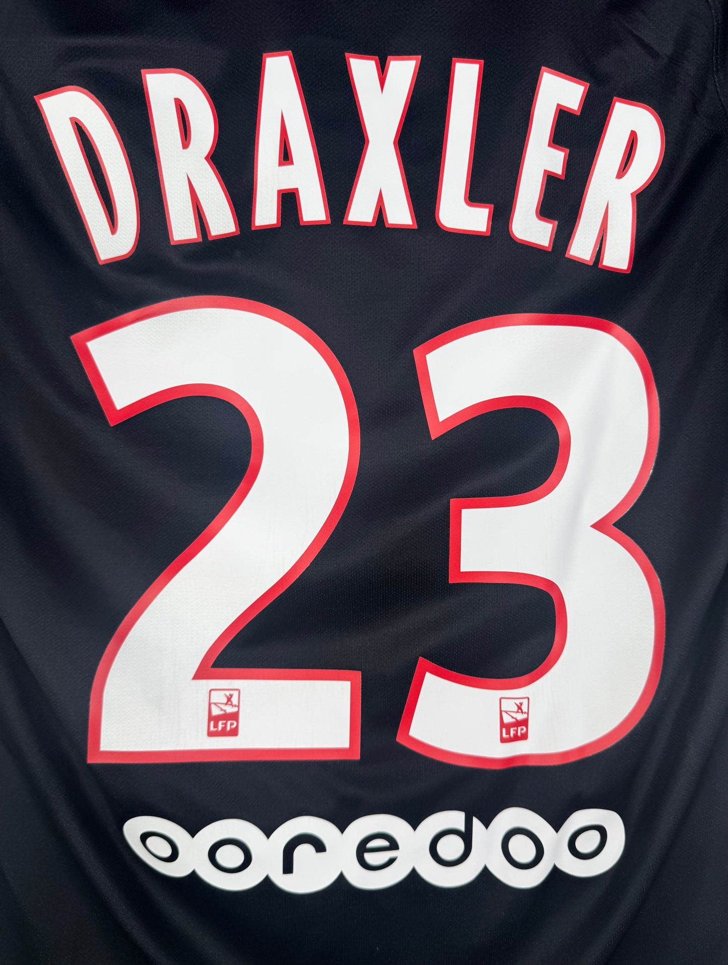 Zoom sur le nom DRAXLER et le numéro 23 en typographie officielle blanche à contours rouges.