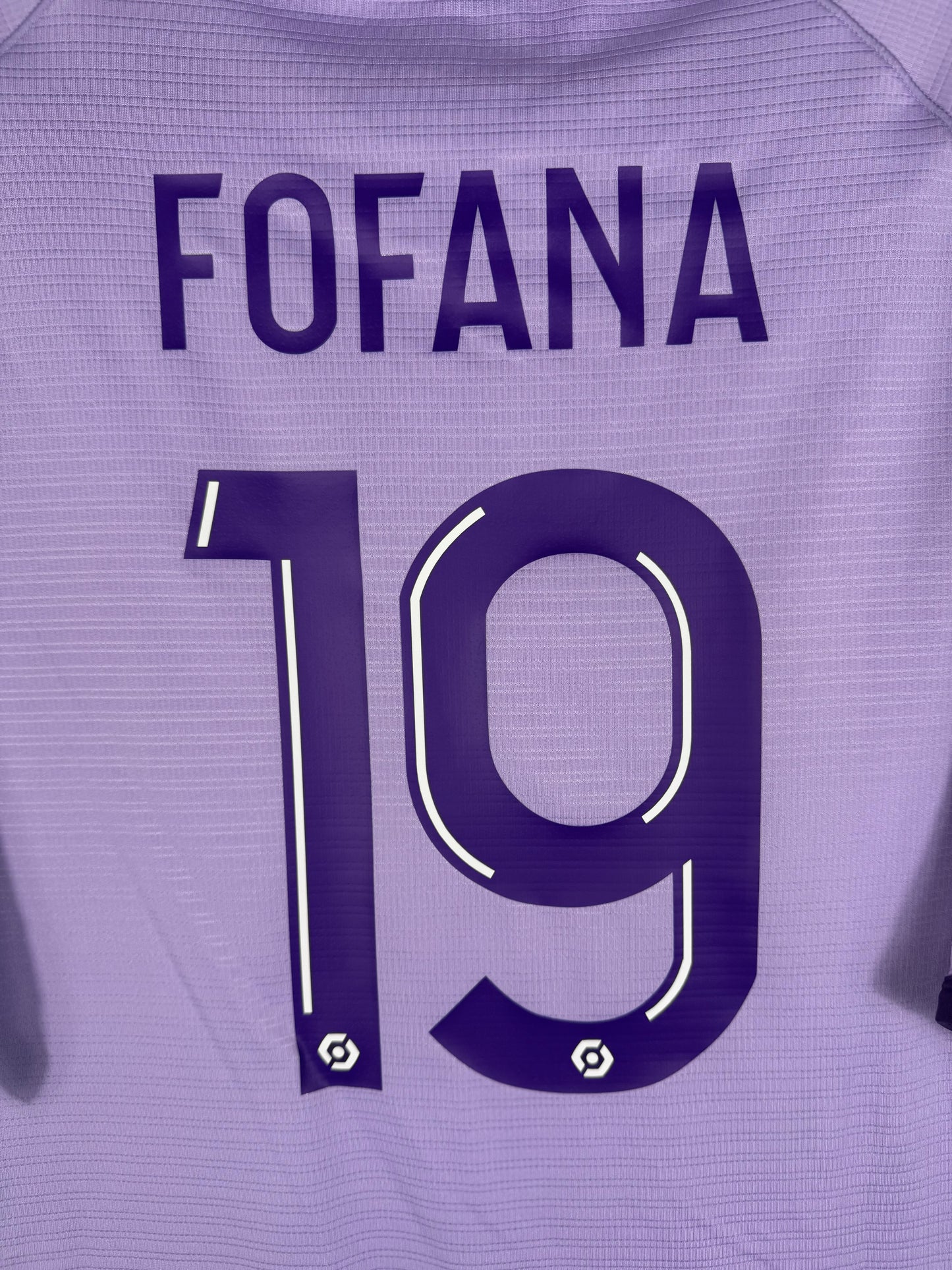 Zoom sur le nom FOFANA et le numéro 19 violet foncé avec bordure blanche