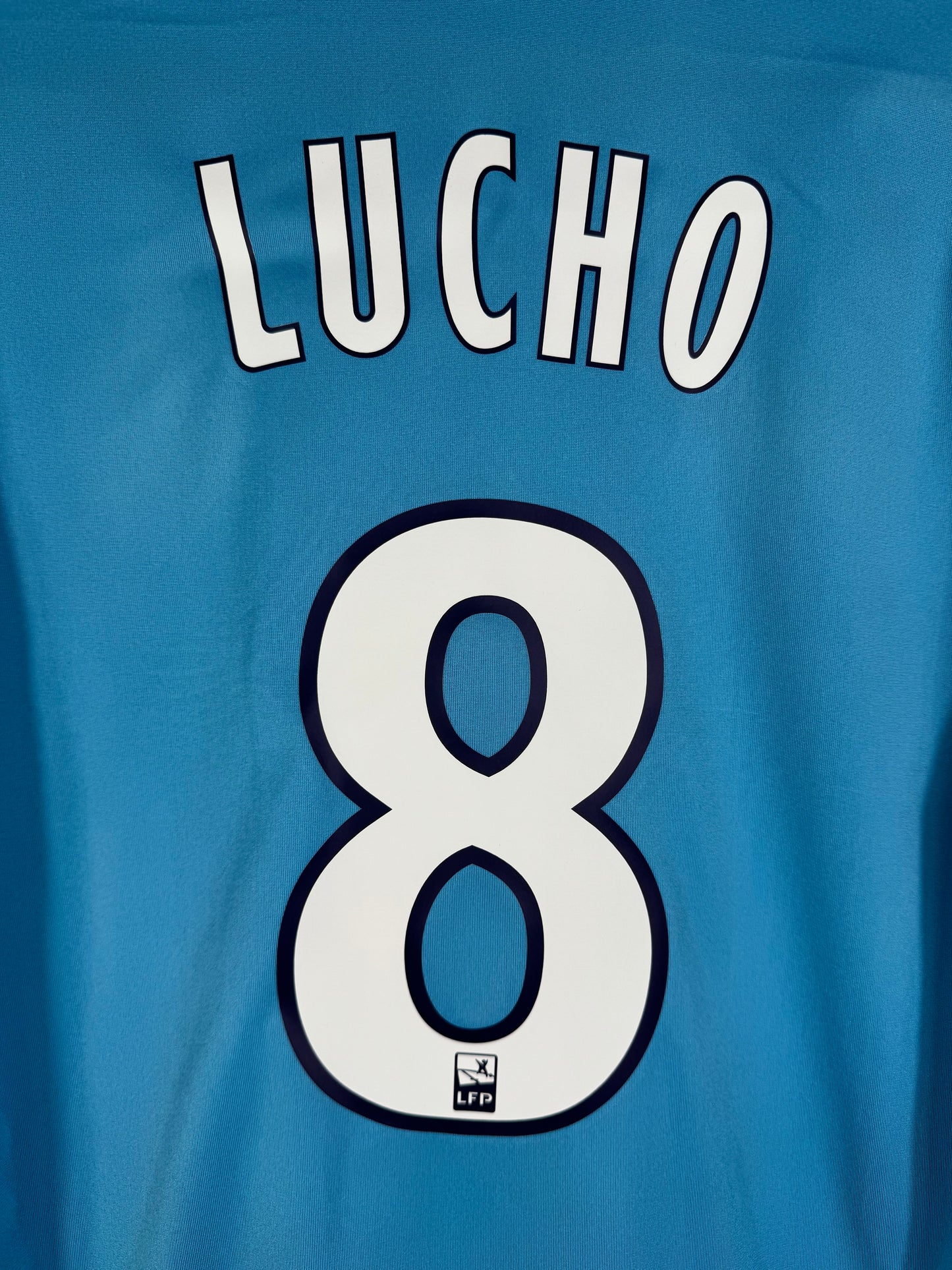 Zoom sur le nom LUCHO et le numéro 8 blanc avec liseré bleu marine et logo de l'OM intégré.