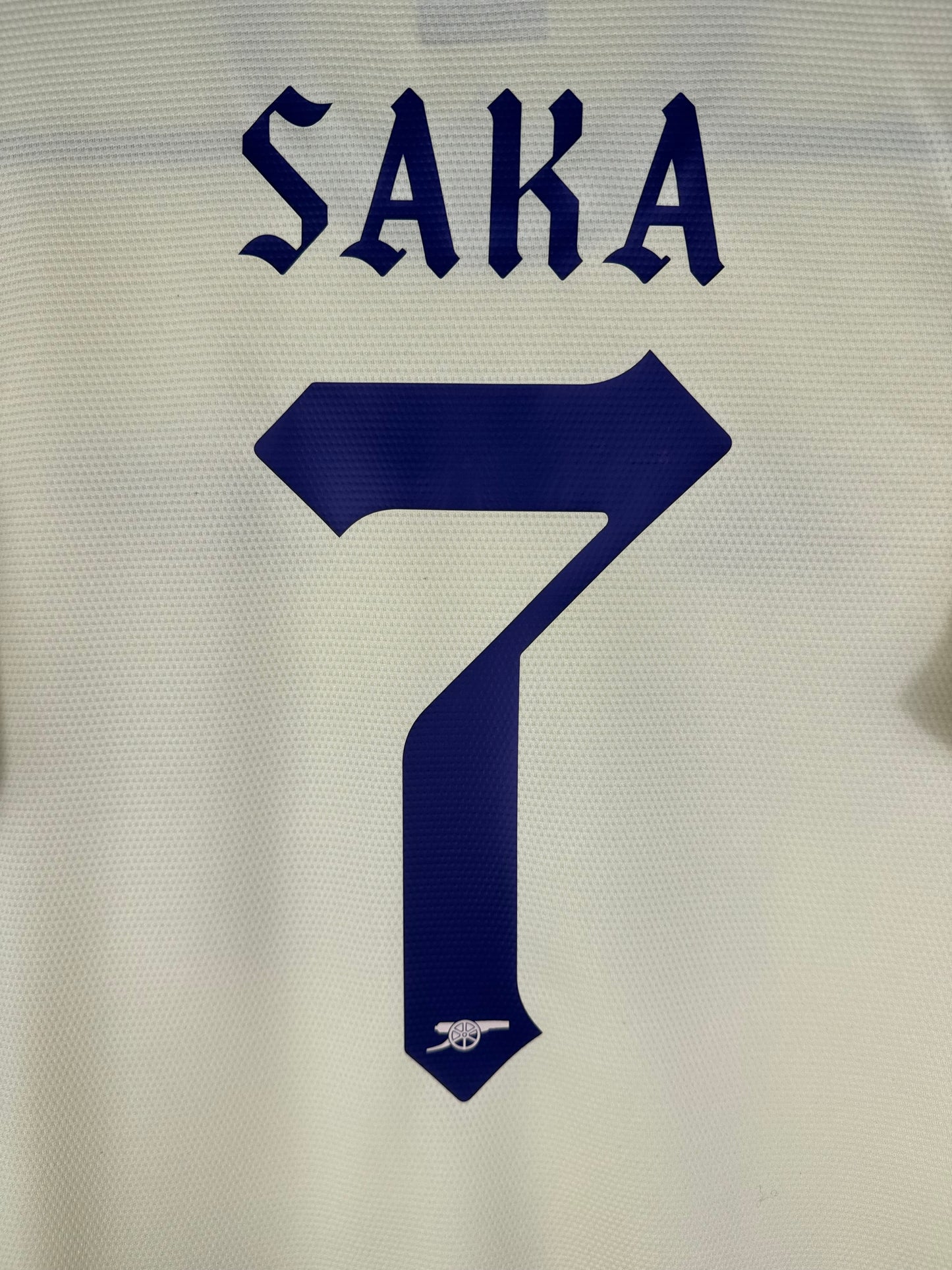 Zoom sur le nom SAKA et le numéro 7 bleu marine, typographie gothique officielle d'Arsenal pour les coupes 2021-2022.