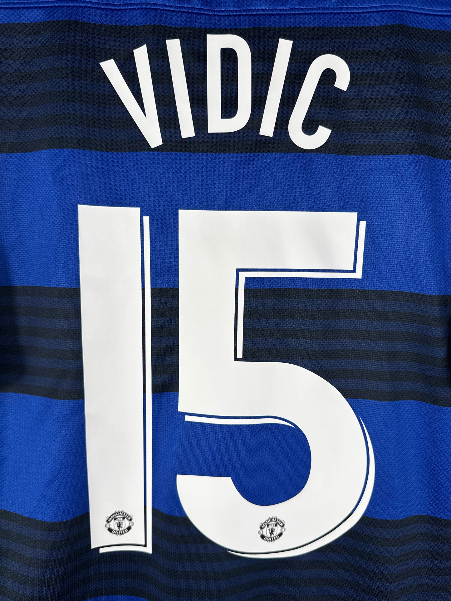 Zoom sur le nom VIDIC et le numéro 15 blanc avec le diable rouge intégré dans la base du chiffre, police Coupe d'Europe.