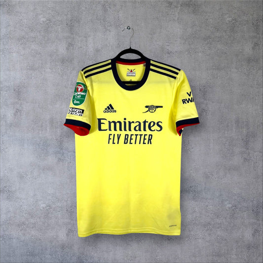 Vue de face du maillot Arsenal Extérieur 2021/22 jaune perle avec logo Canon rétro bleu marine et sponsor Emirates.