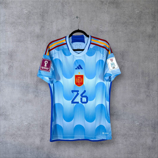 Vue de face du maillot Espagne Extérieur 2022 bleu ciel avec motifs de vagues, écusson centré et numéro 26.