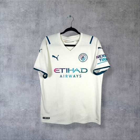 Maillot Manchester City 2021-2022 extérieur de face, blanc cassé à finitions bleu canard, sponsor Etihad irisé