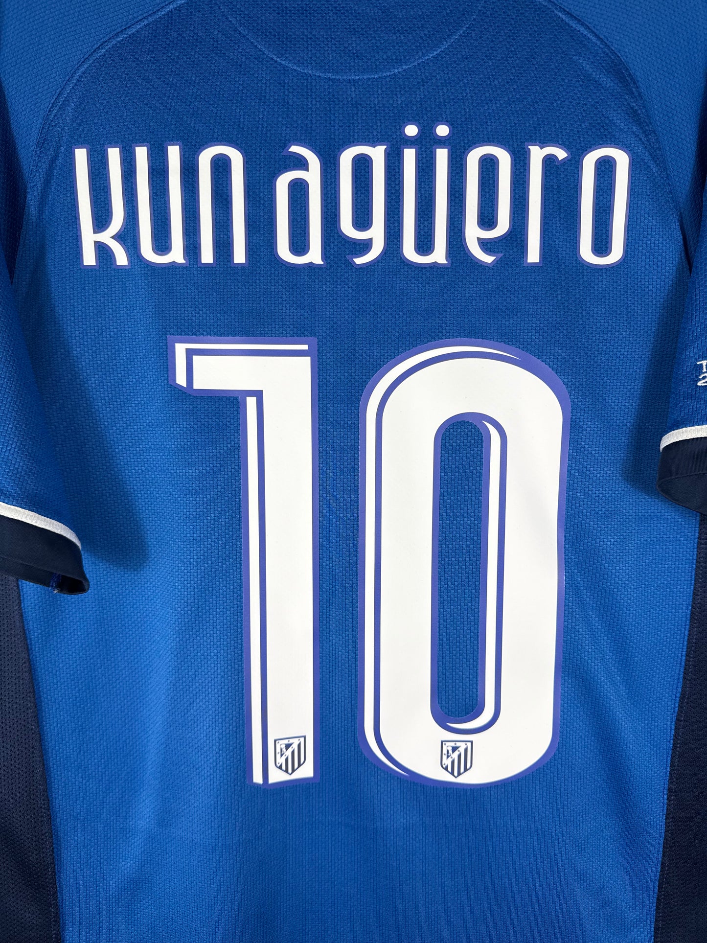 Zoom sur le nom KUN AGÜERO et le numéro 10 blanc avec liseré marine, typographie officielle Atletico Madrid 2007-2008.