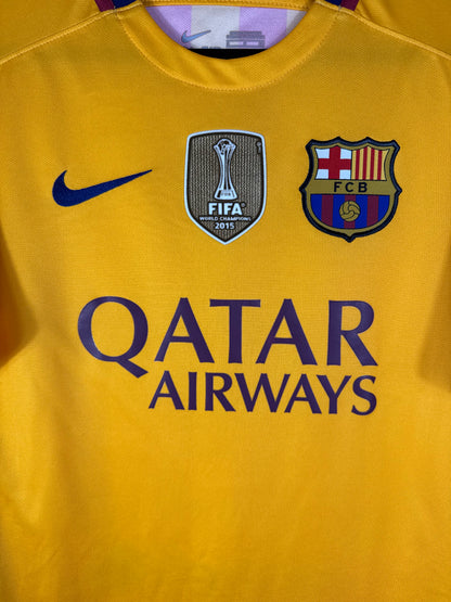 Gros plan sur l'écusson du FC Barcelone, le badge FIFA World Champions doré et le logo Nike bleu sur fond jaune.