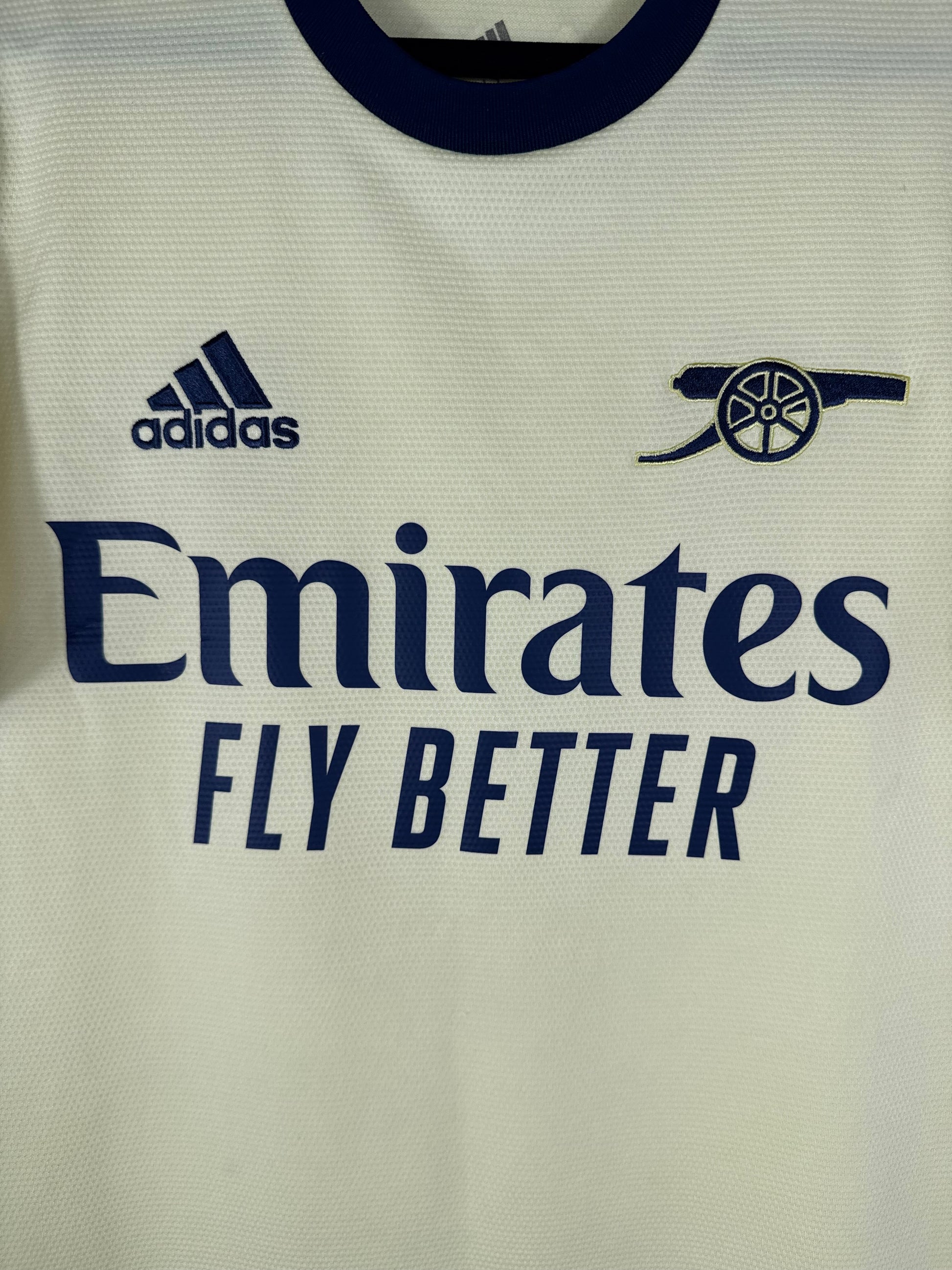 Gros plan sur le logo Canon rétro d'Arsenal et le logo Adidas bleu marine sur le tissu jaune perle.