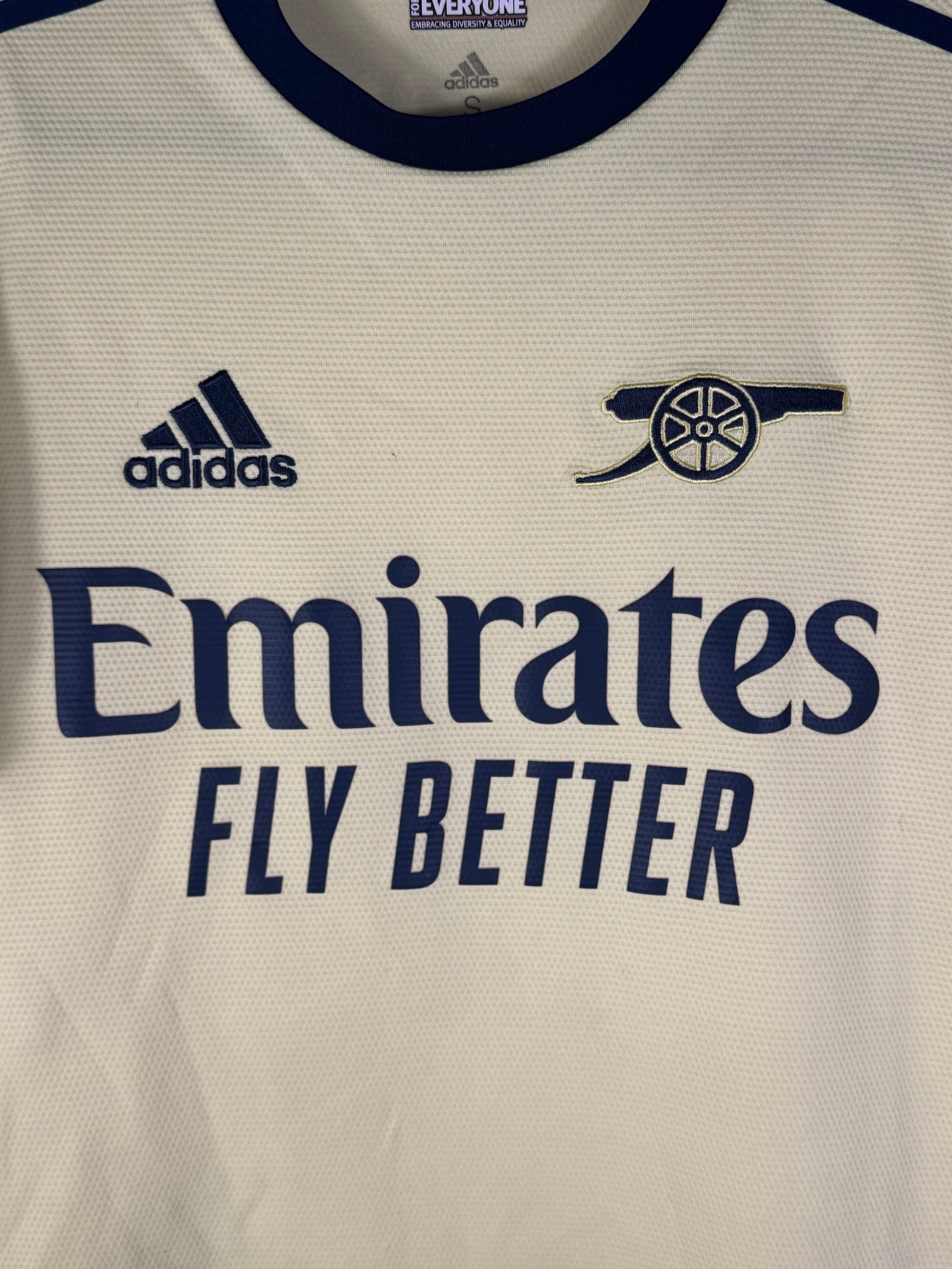 Gros plan sur le logo Canon rétro d'Arsenal et le logo Adidas bleu marine sur le tissu jaune perle.