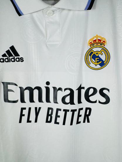 Gros plan sur le col à bouton, le logo Adidas noir et l'écusson du Real Madrid sur le tissu blanc.