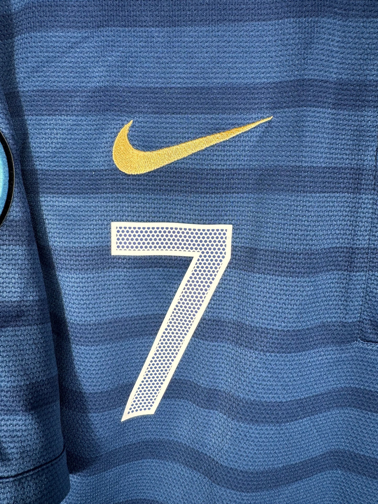 Gros plan sur l'écusson de la Fédération Française de Football et le swoosh Nike brodés en doré.