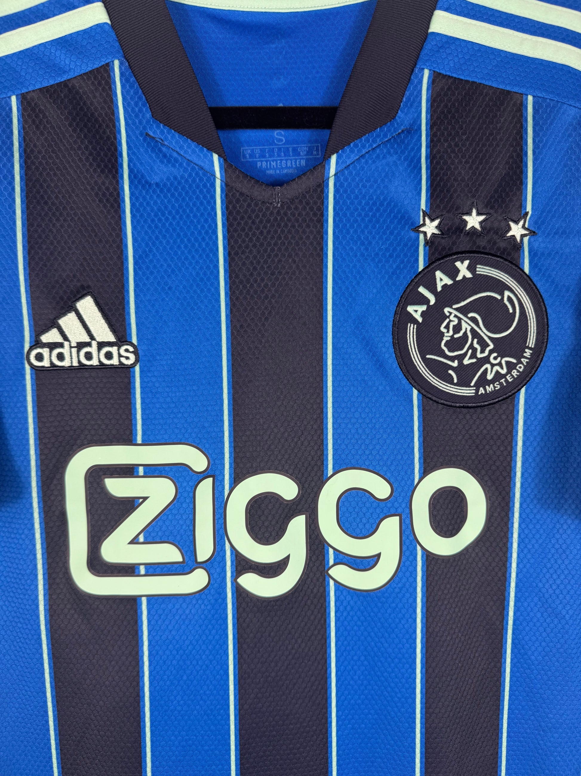 Gros plan sur l'écusson de l'Ajax, le logo Adidas et les rayures verticales.