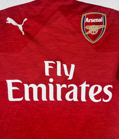 Gros plan sur l'écusson des Gunners et le sponsor Fly Emirates sur fond rouge chiné.