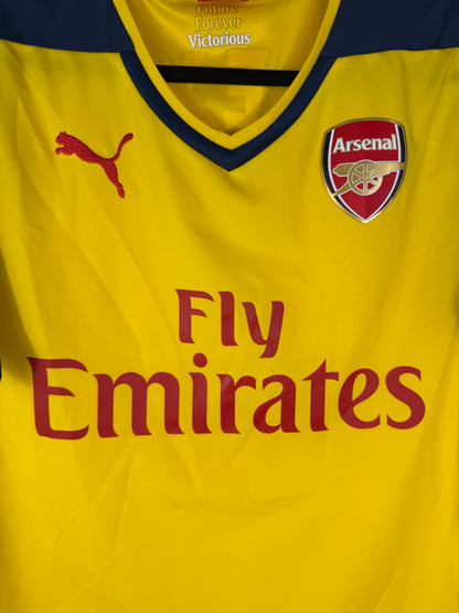 Gros plan sur l'écusson d'Arsenal brodé et le logo Puma rouge sur le torse jaune.