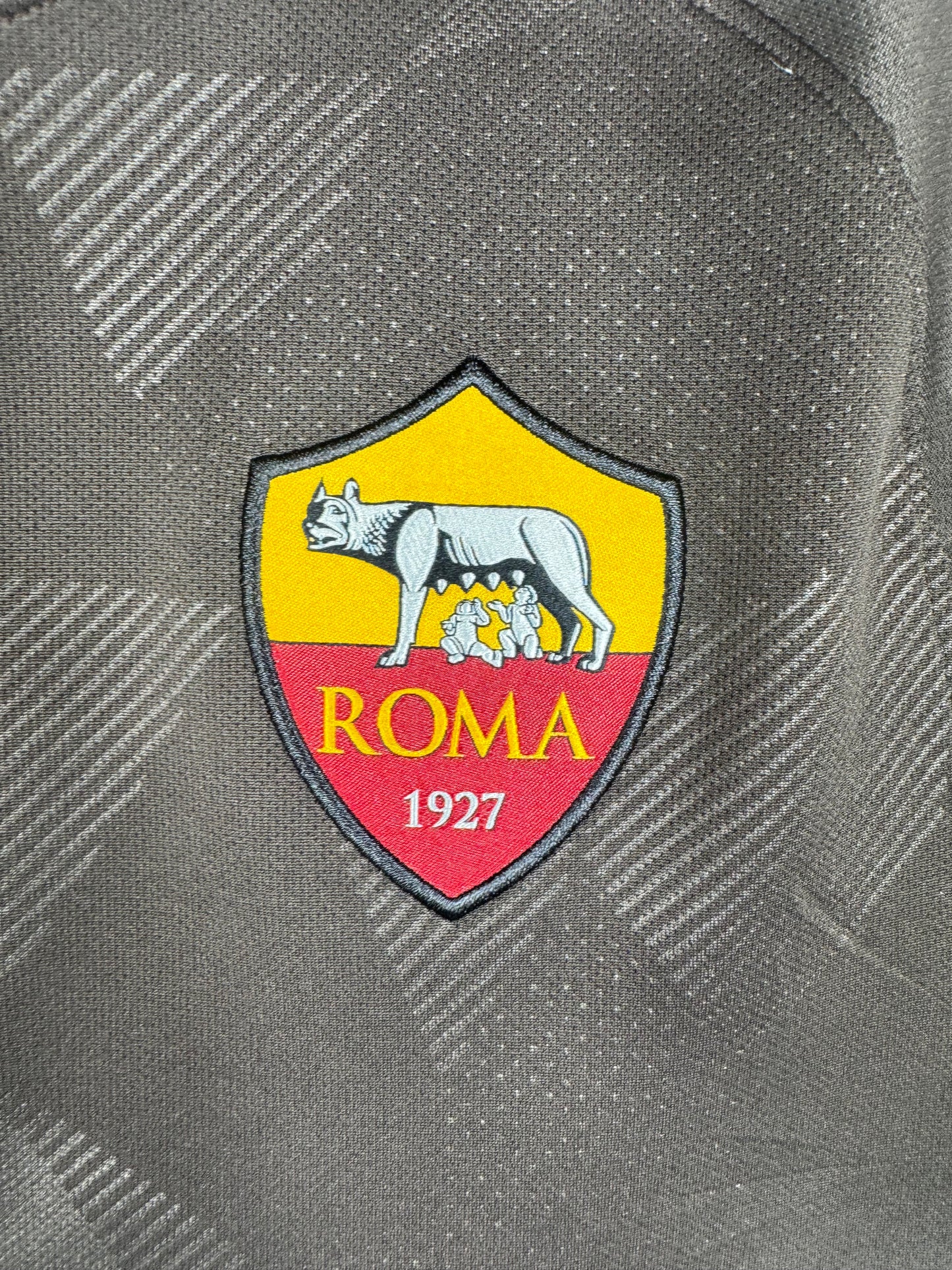 Gros plan sur l'écusson AS Roma et le motif texturé du tissu.