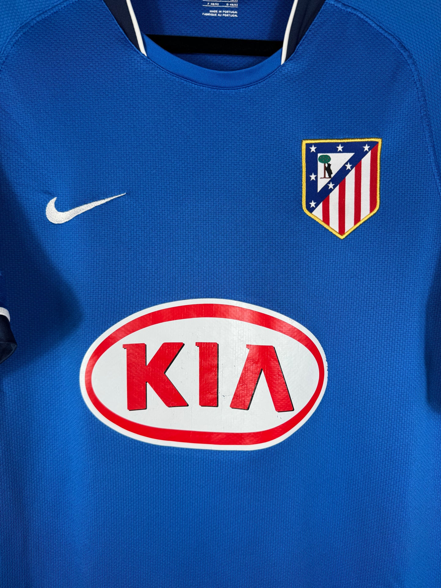 Gros plan sur l'écusson de l'Atletico Madrid et le sponsor KIA sur le maillot extérieur bleu.