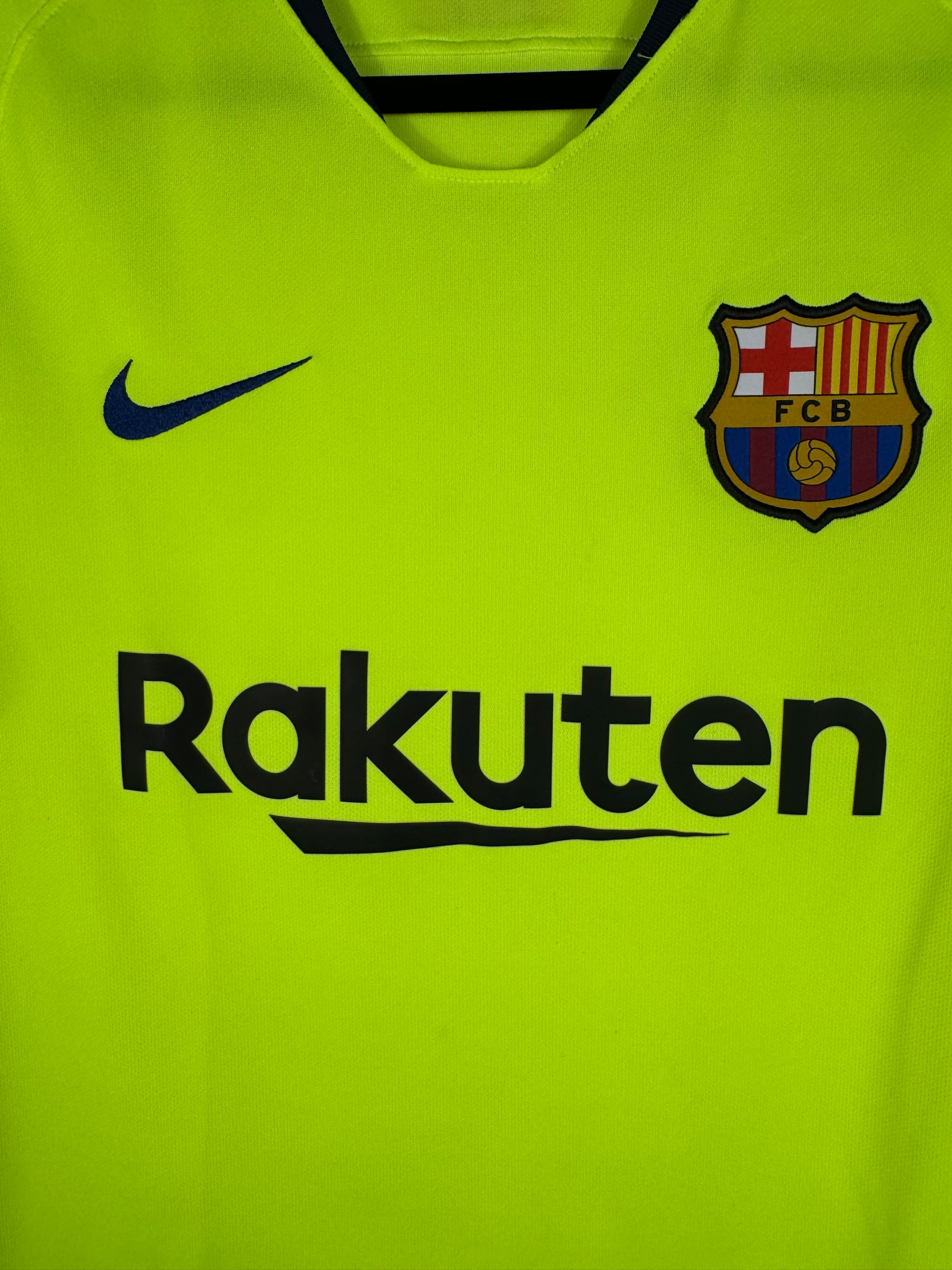 Gros plan sur l'écusson du FC Barcelone et le swoosh Nike bleu sur fond jaune fluo.