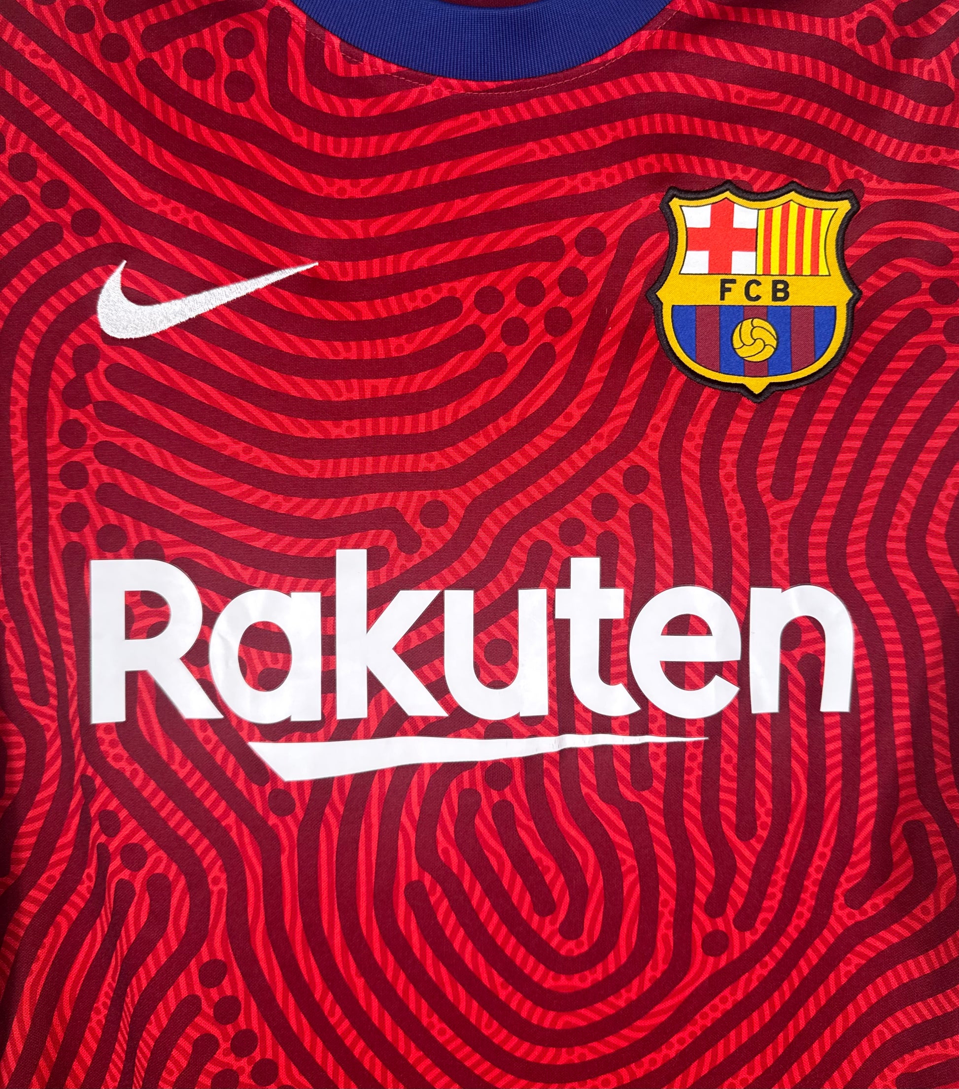 Gros plan sur l'écusson FC Barcelone et logo Nike sur motif abstrait rouge.