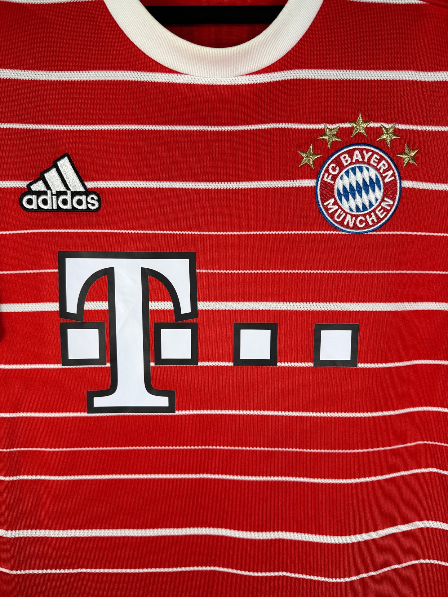 Gros plan sur l'écusson du Bayern Munich aux 5 étoiles et le logo Adidas blanc sur le tissu rouge.