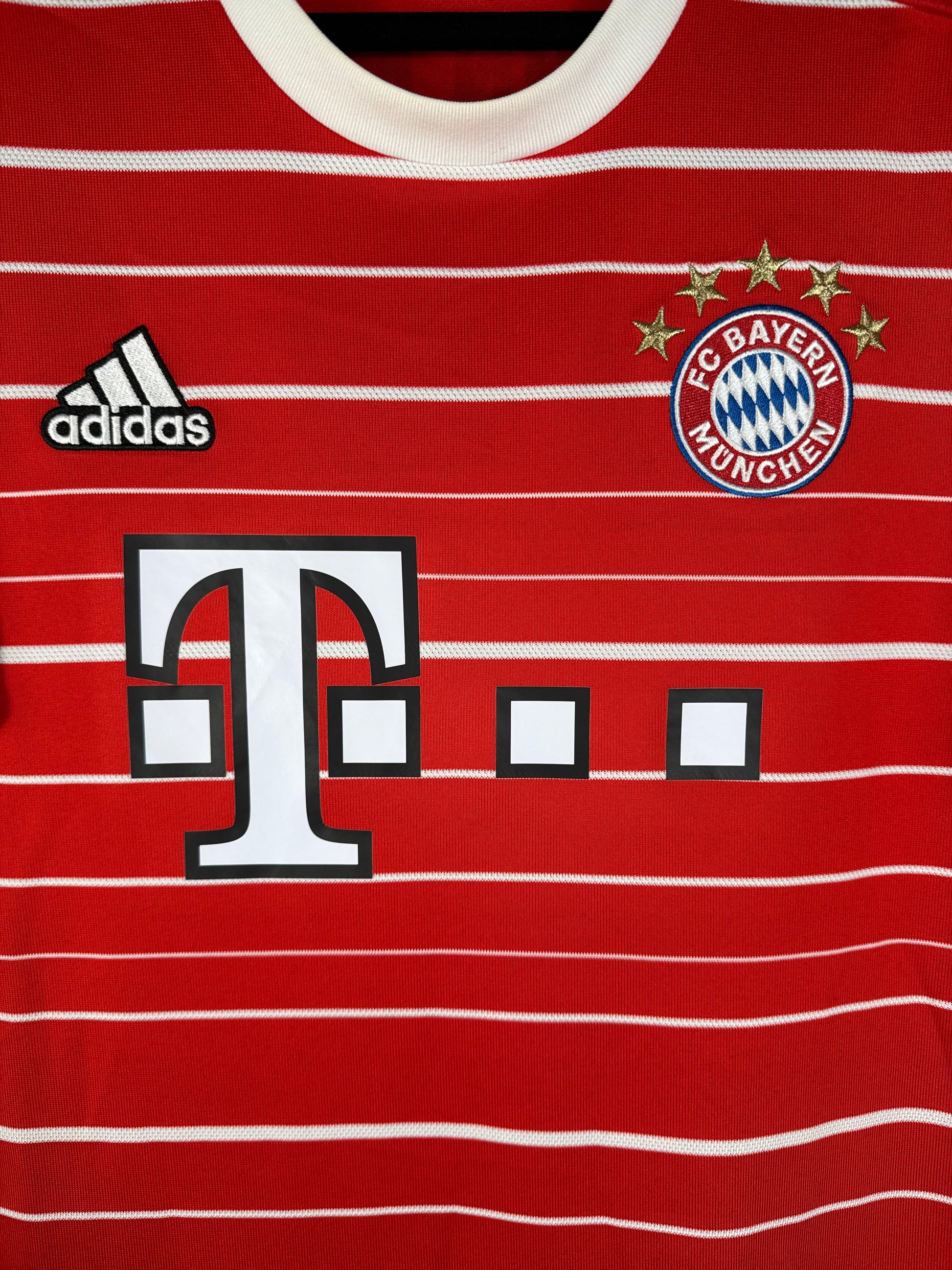 Gros plan sur l'écusson du Bayern Munich aux 5 étoiles et le logo Adidas blanc sur le tissu rouge.