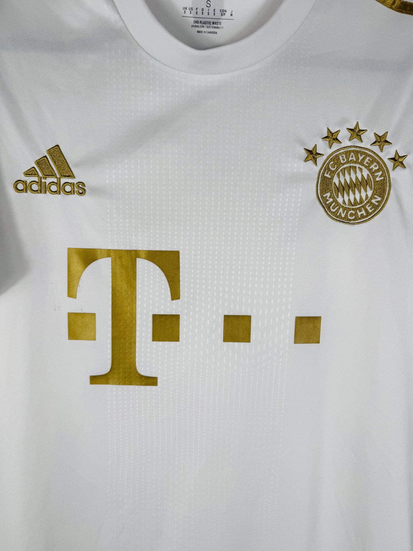 Gros plan sur l'écusson du Bayern Munich et le logo Adidas dorés sur le tissu blanc.