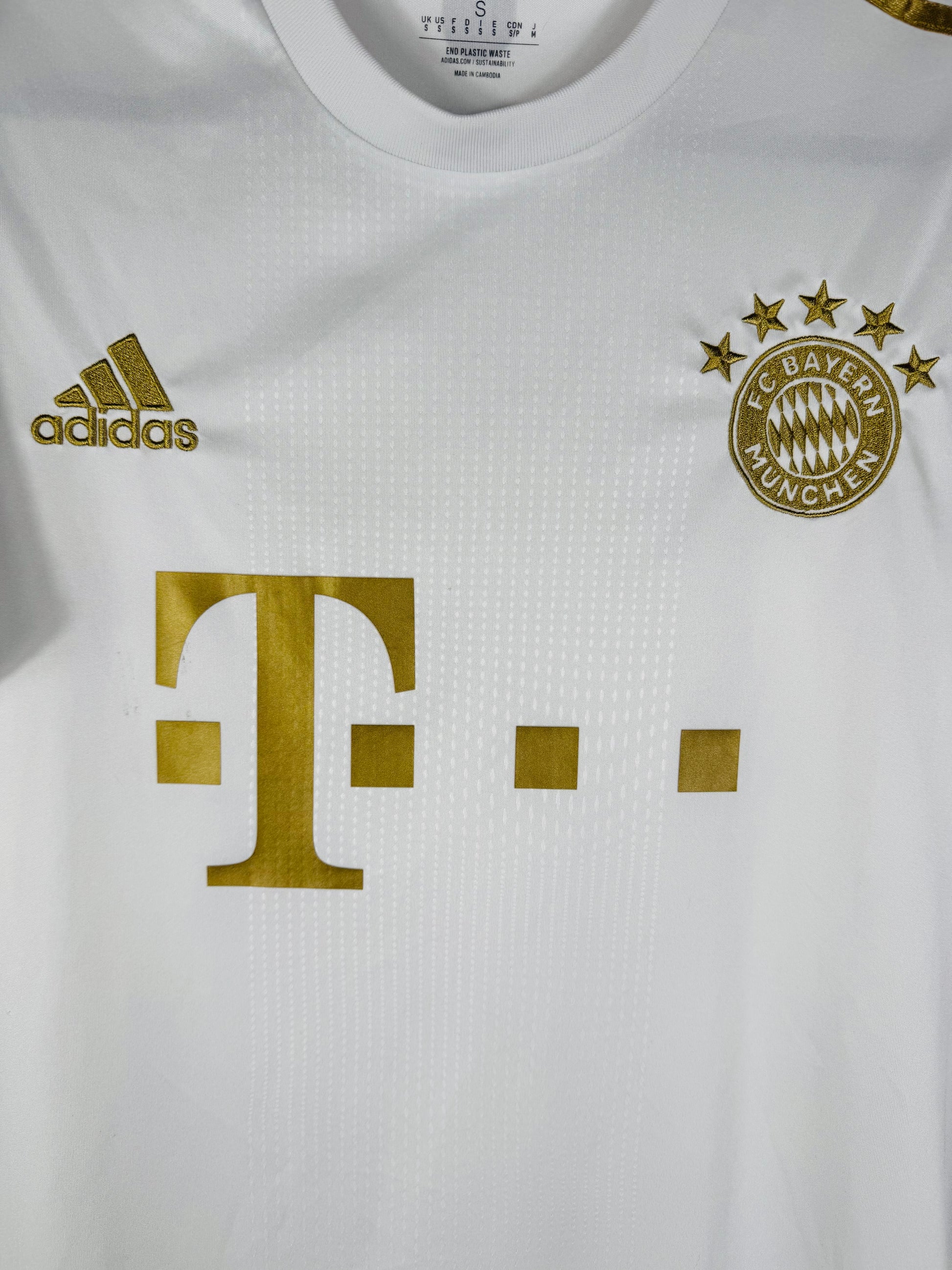 Gros plan sur l'écusson du Bayern Munich et le logo Adidas dorés sur le tissu blanc.