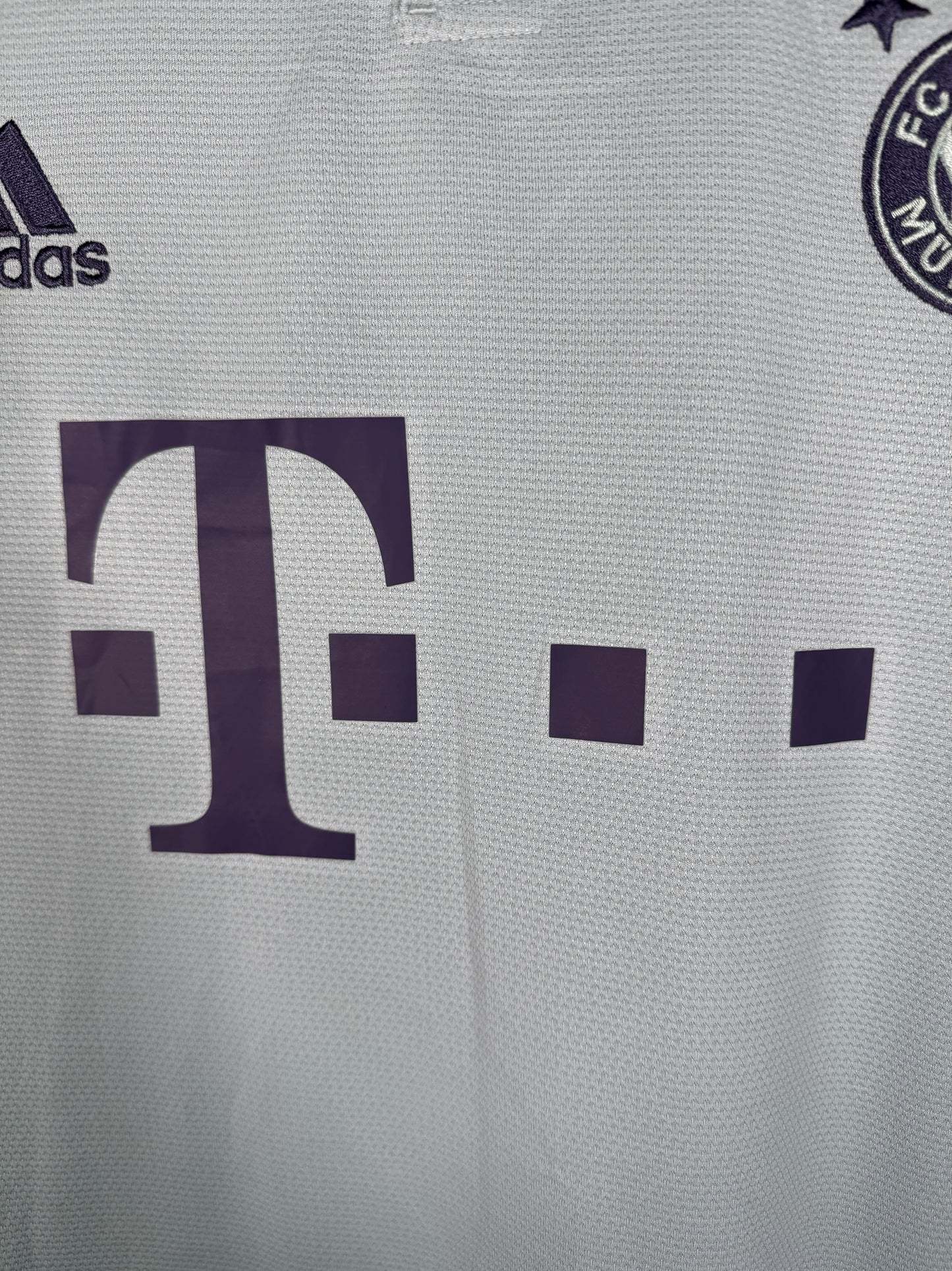 Gros plan sur l'écusson monochrome du Bayern et le sponsor T-Mobile violet.