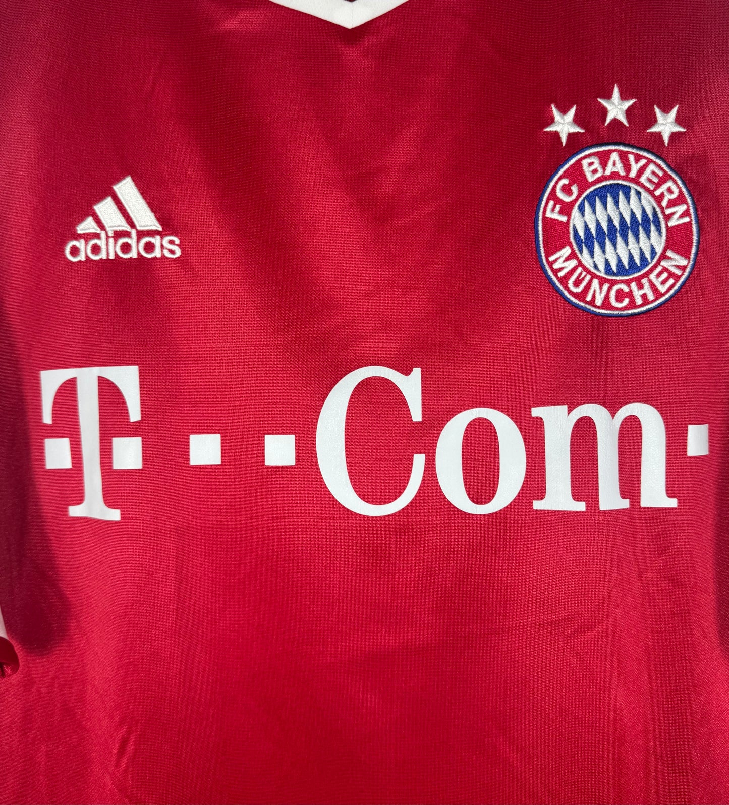 Gros plan sur l'écusson 3 étoiles du Bayern, le logo Adidas et le sponsor T-Com ··.
