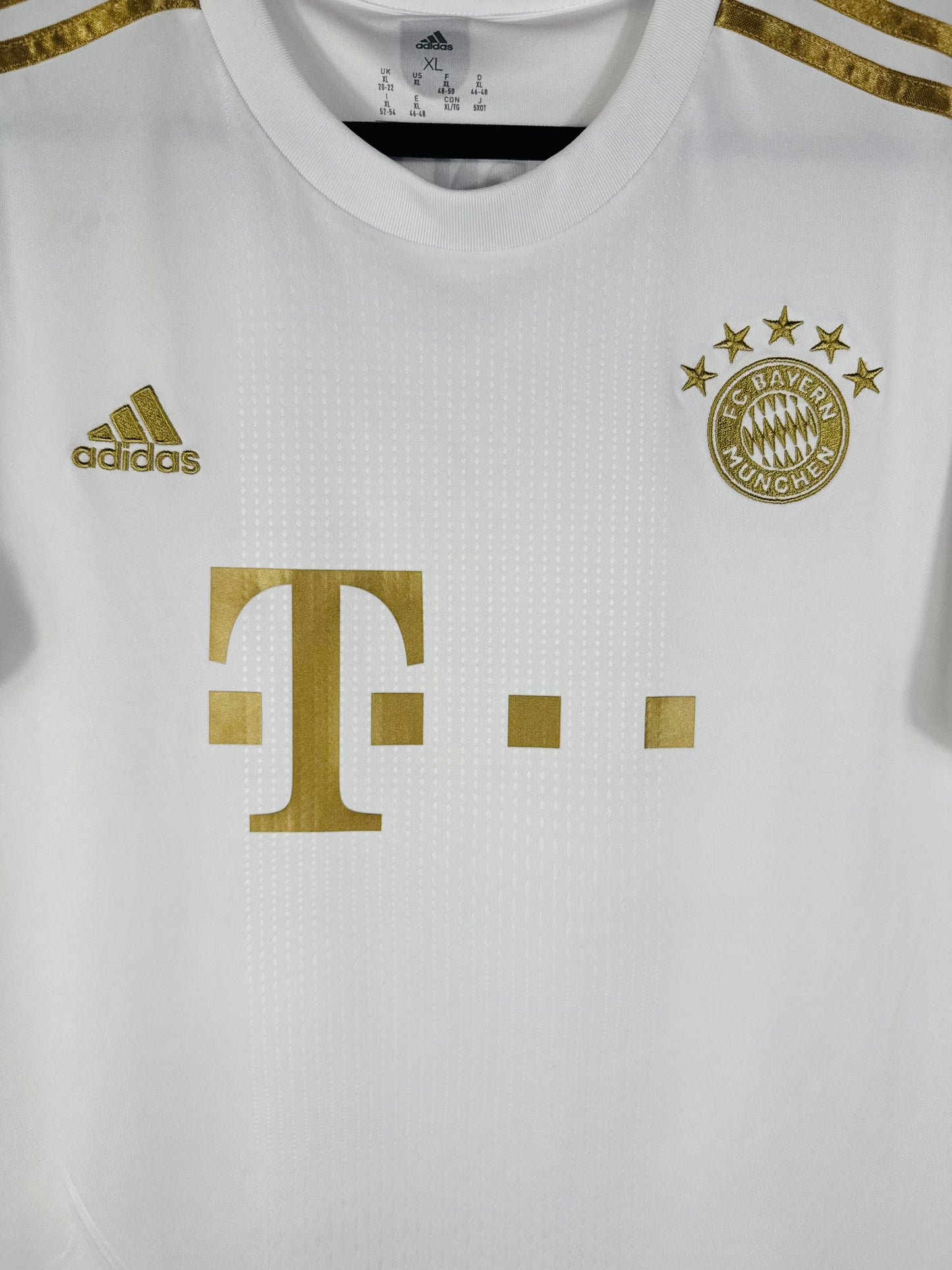 Gros plan sur l'écusson du Bayern Munich aux 5 étoiles et le logo Adidas brodés en or métallique.