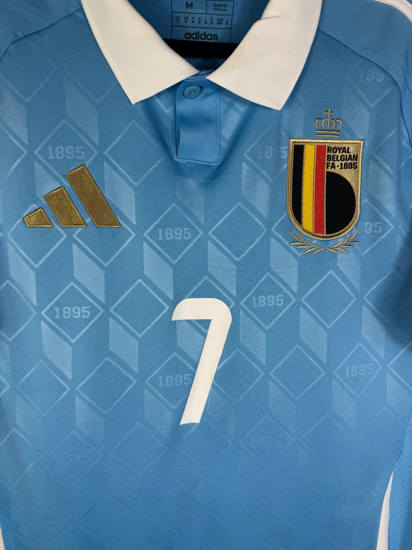 Gros plan sur l'écusson de la sélection belge et le logo Adidas doré sur le maillot avec le numéro 7 au centre.