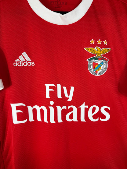 Gros plan sur l'écusson du SL Benfica, le logo Adidas blanc et le sponsor Fly Emirates sur le tissu rouge.