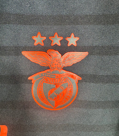 Gros plan sur l'écusson texturé du Benfica Lisbonne et les 3 étoiles sur maillot noir.