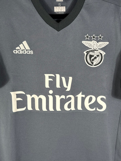 Gros plan sur l'écusson monochrome blanc du Benfica Lisbonne et le logo Adidas brodé sur le tissu gris.