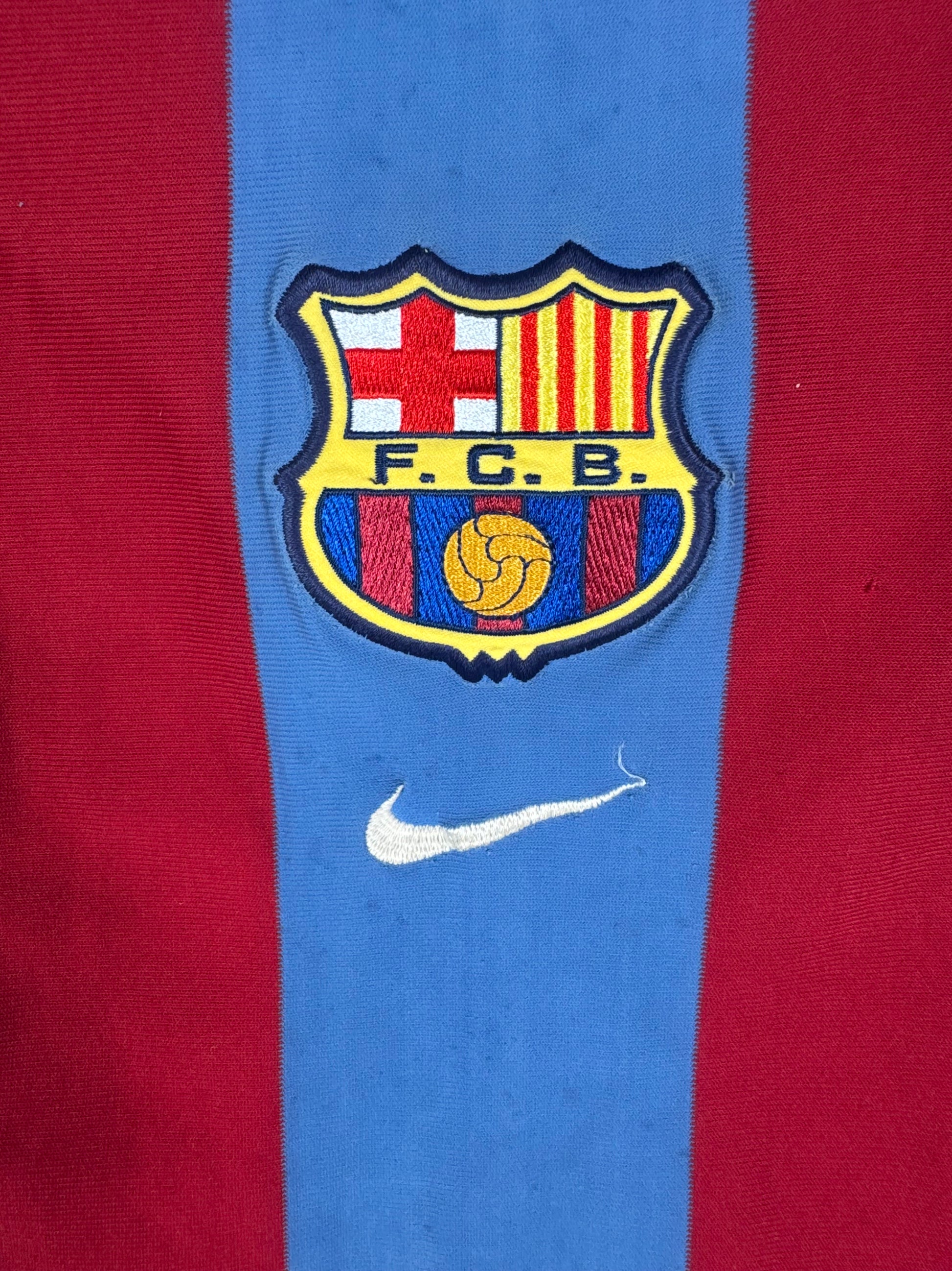 Gros plan sur l'écusson historique du FC Barcelone et le logo Nike blanc placés au centre du maillot.