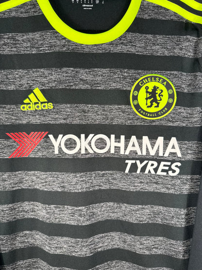 Gros plan sur l'écusson de Chelsea monochrome et le logo Adidas jaune fluo sur fond chiné.