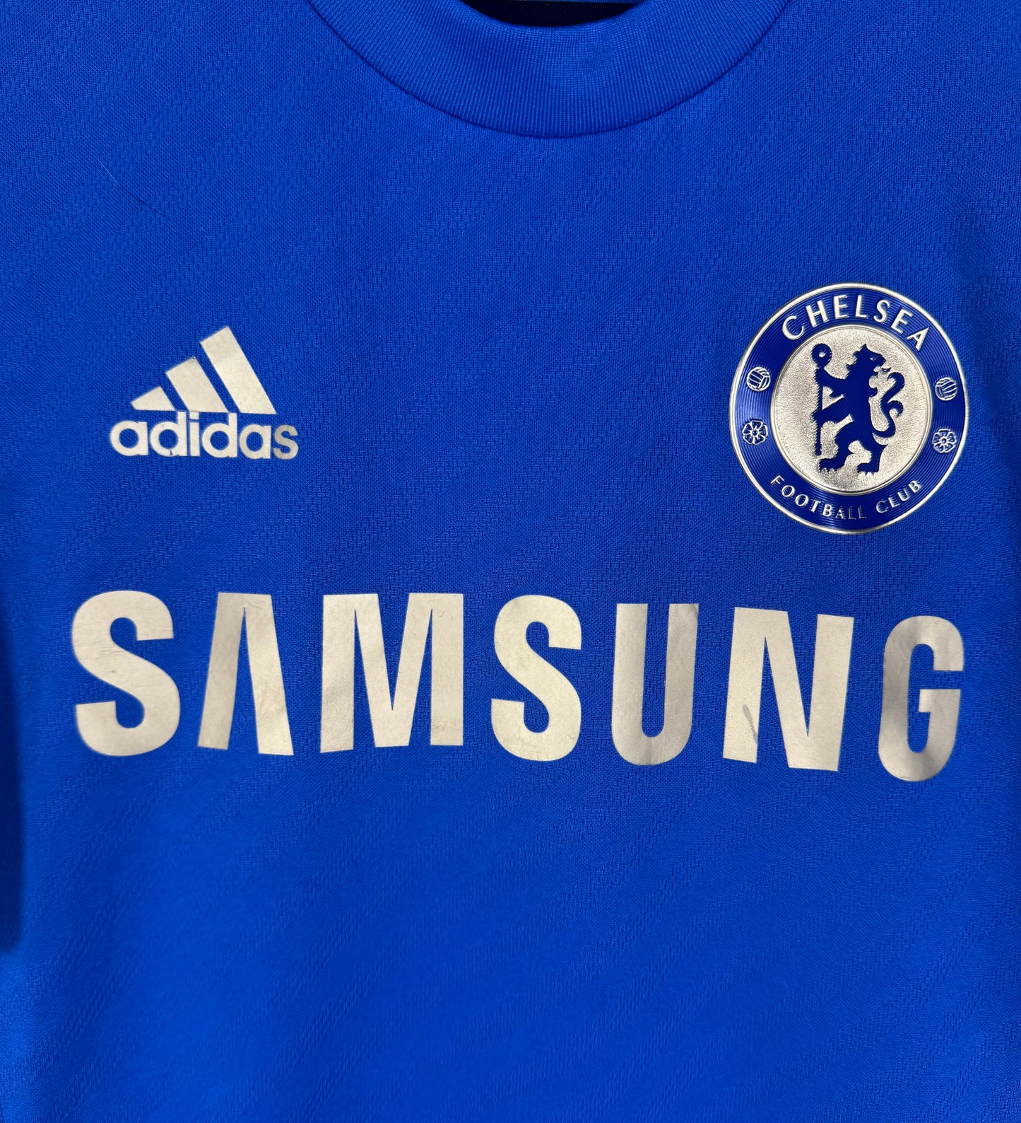 Gros plan sur le sponsor Samsung doré et l'écusson brodé du Chelsea FC.