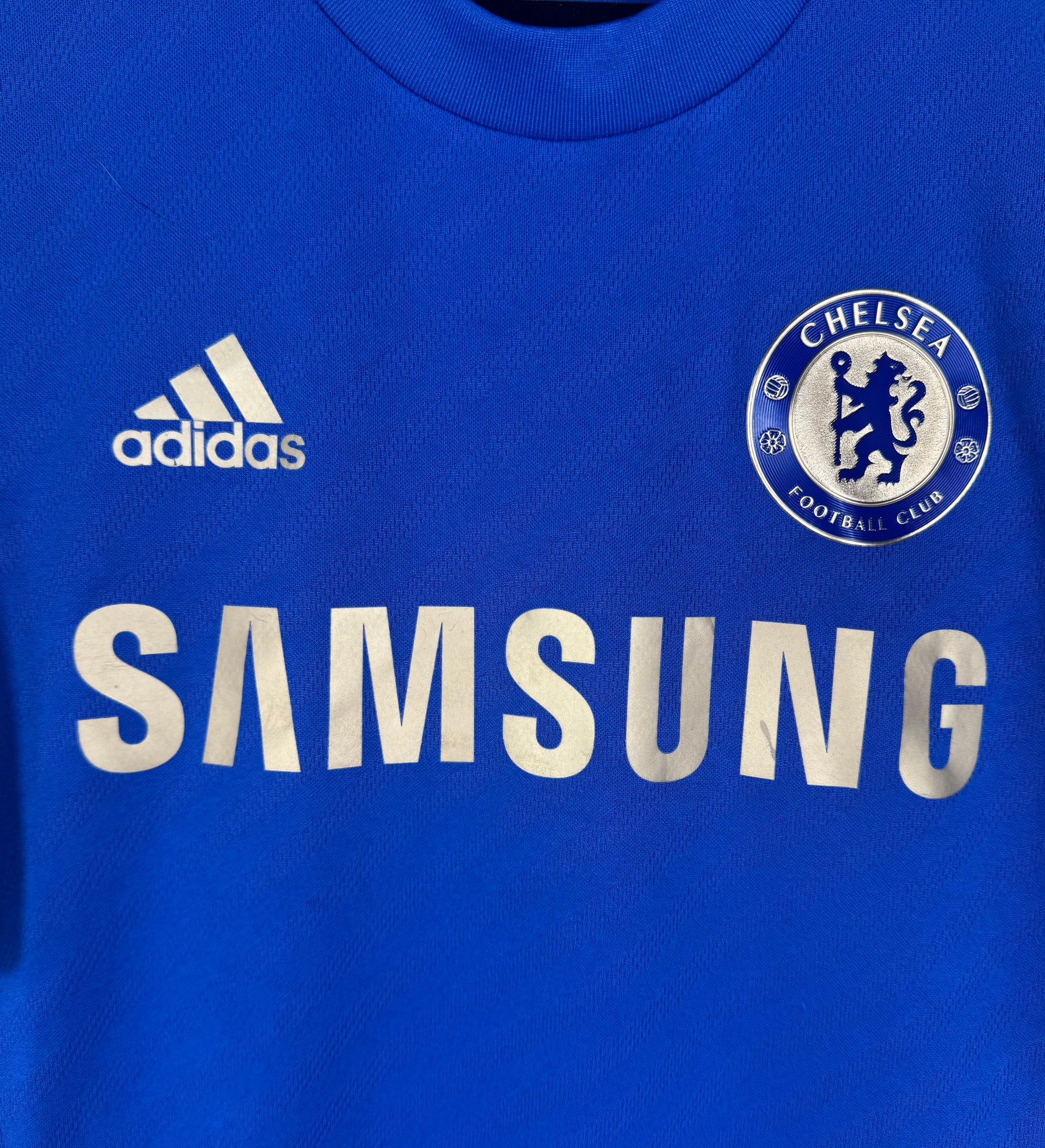Gros plan sur le sponsor Samsung doré et l'écusson brodé du Chelsea FC.