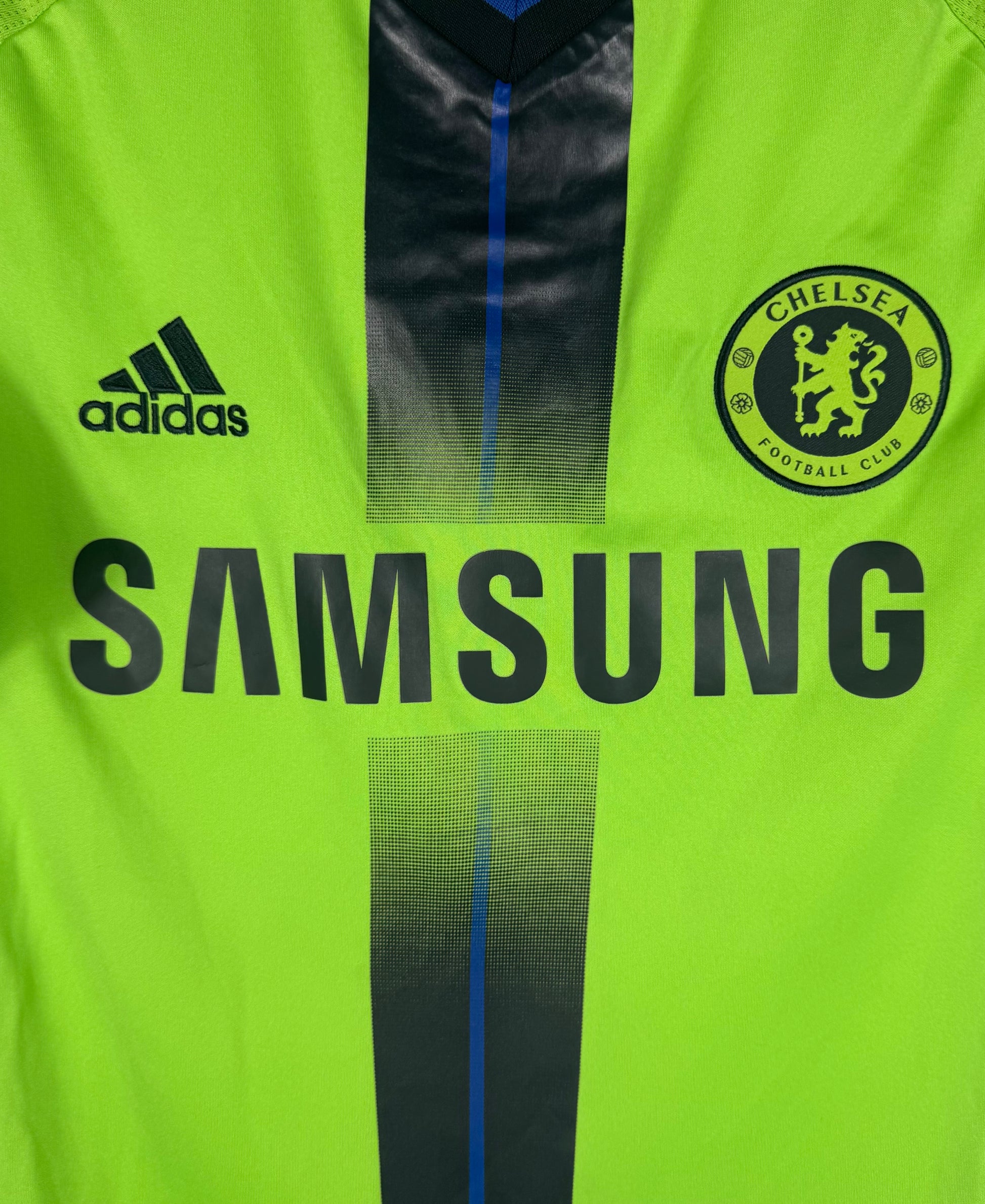 Gros plan sur le sponsor Samsung et l'écusson Chelsea sur le textile vert texturé.