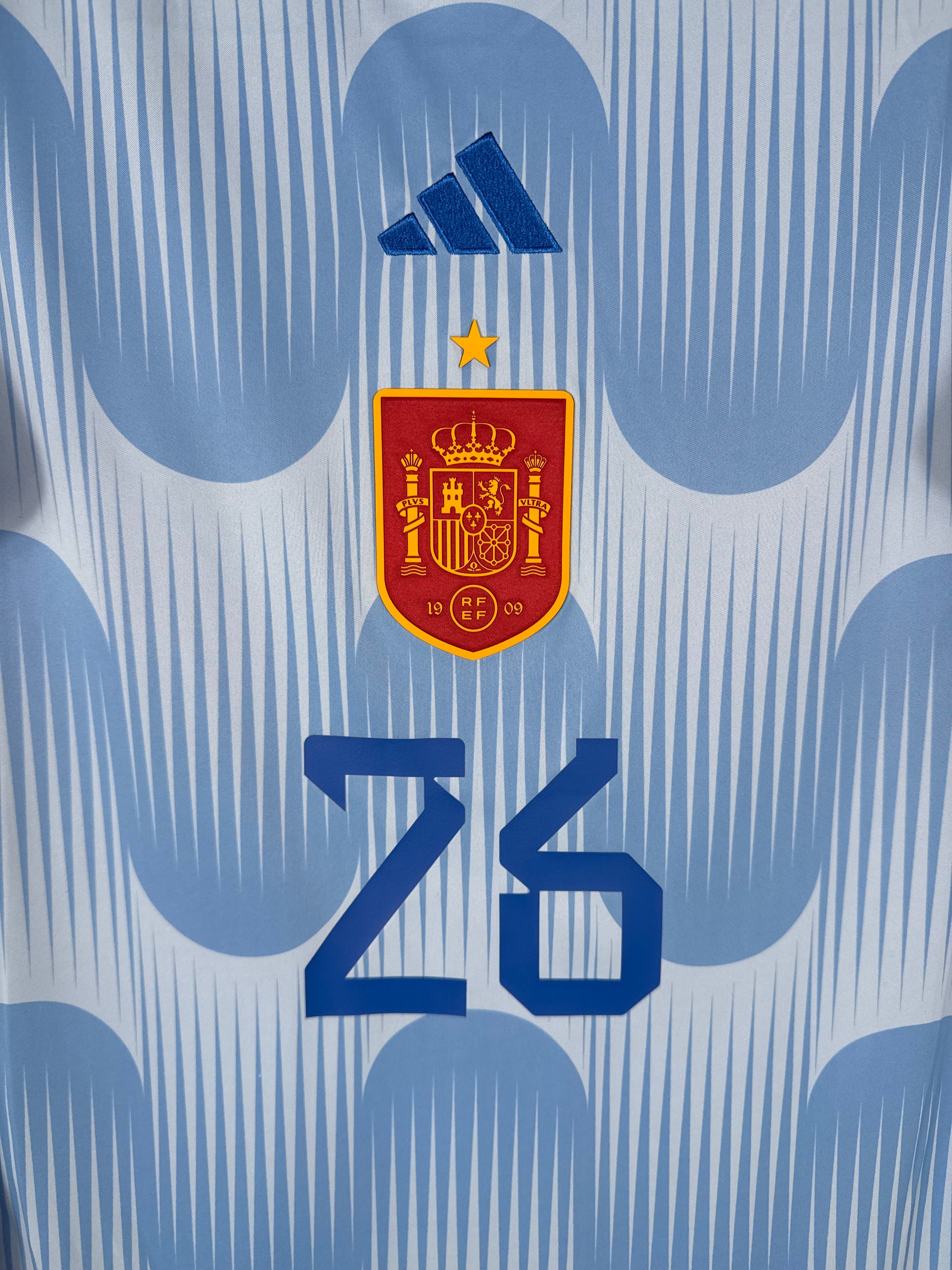 Gros plan sur l'écusson de la sélection espagnole et le logo Adidas bleu marine centrés sur le torse.