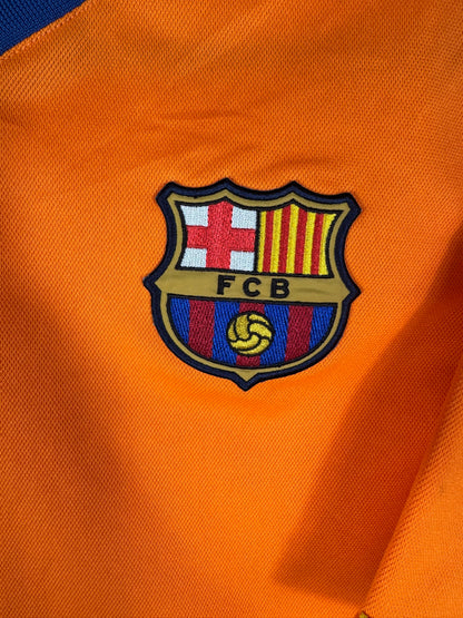 Gros plan sur l'écusson brodé du FC Barcelone sur le torse du maillot extérieur orange.
