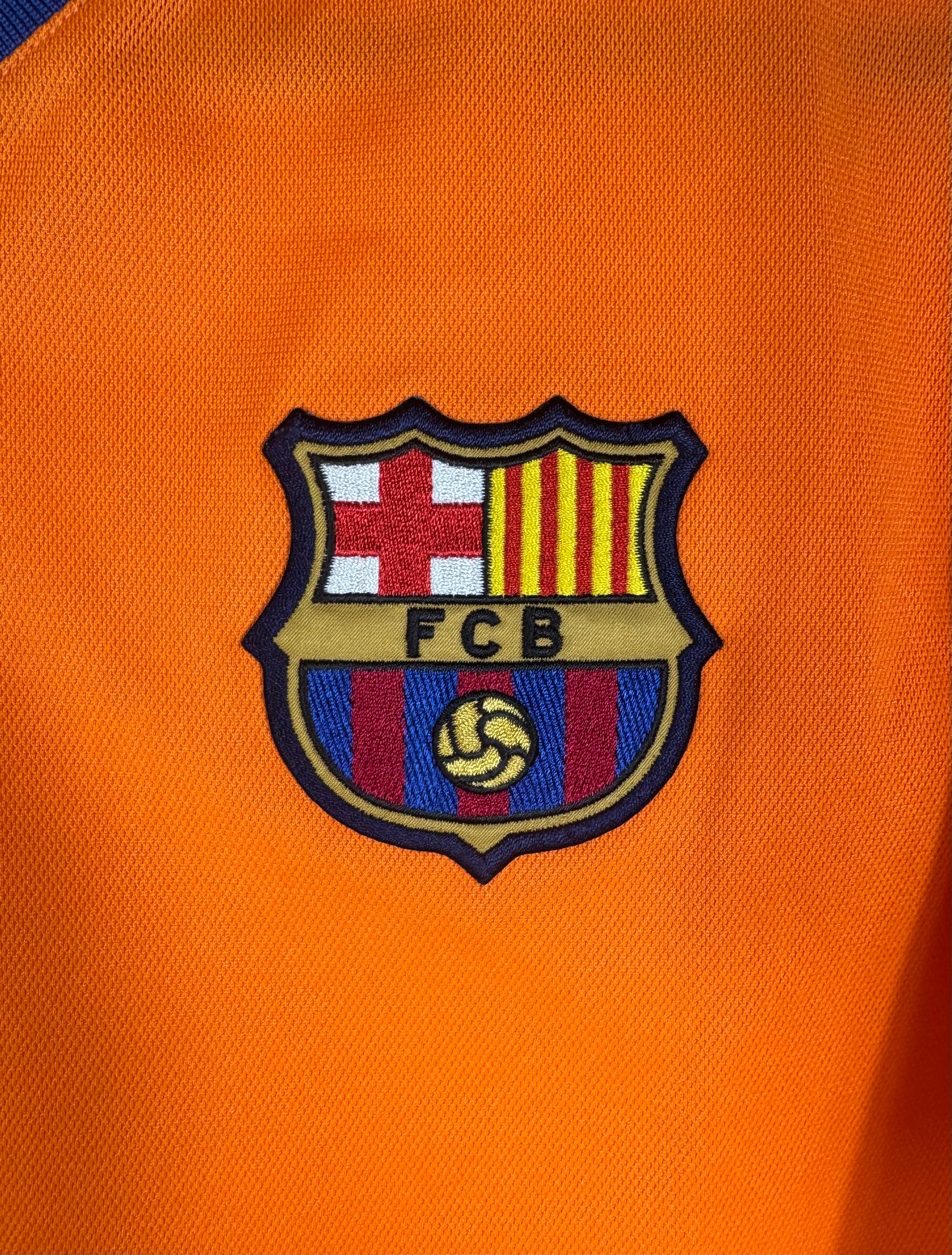 Gros plan sur l'écusson brodé du FC Barcelone sur fond orange vif.