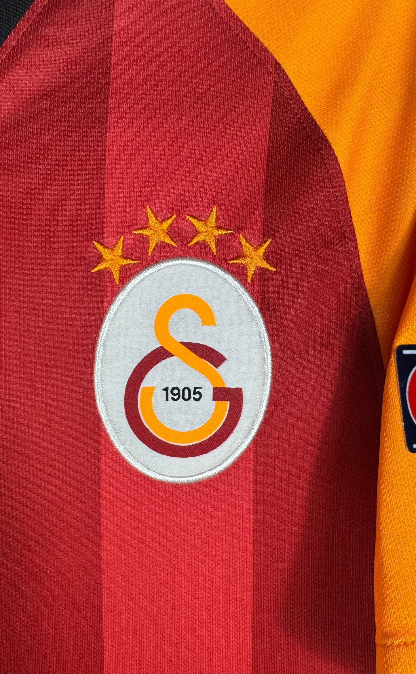 Gros plan sur l'écusson 4 étoiles de Galatasaray sur fond rouge et orange.