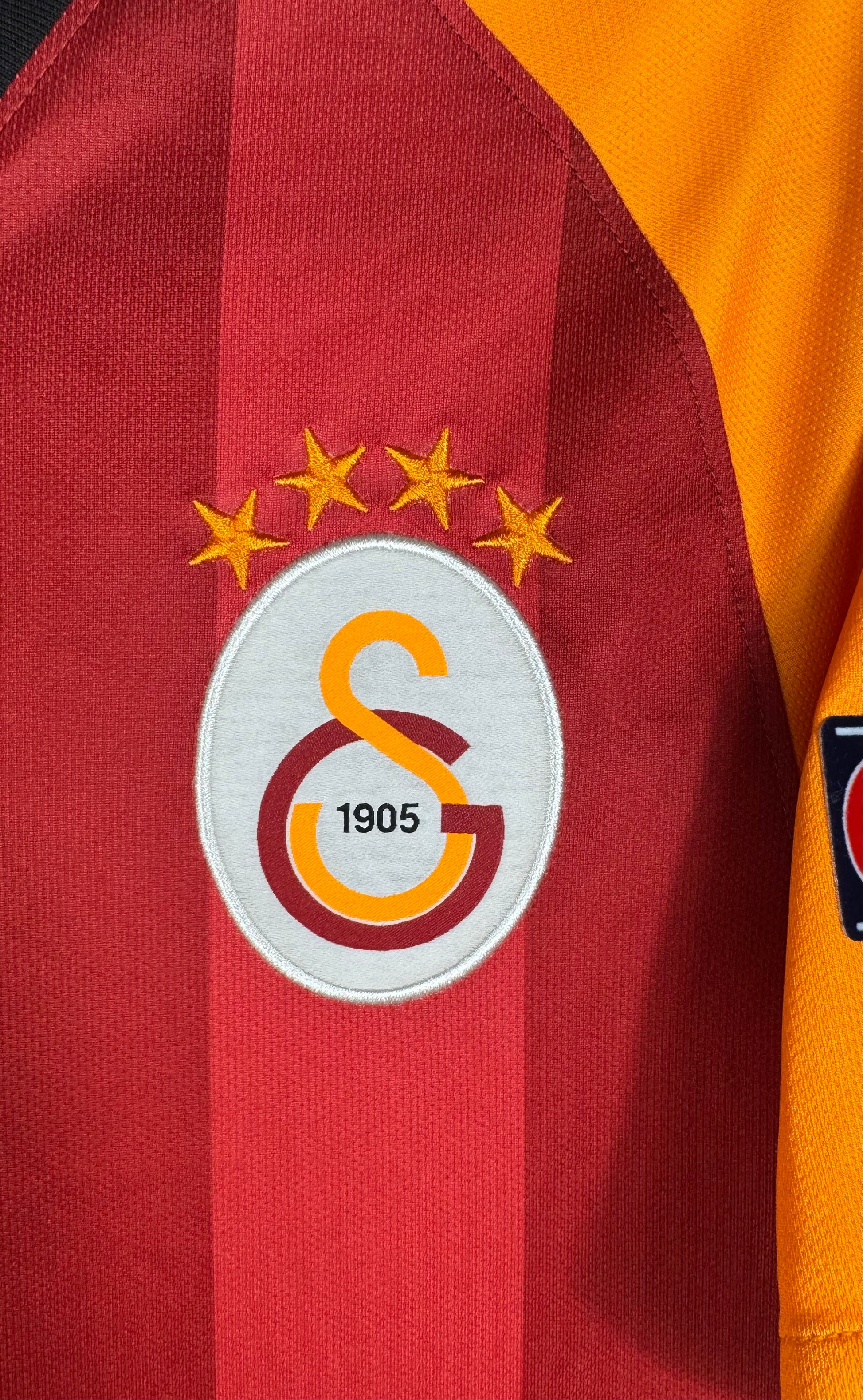 Gros plan sur l'écusson 4 étoiles de Galatasaray sur fond rouge et orange.