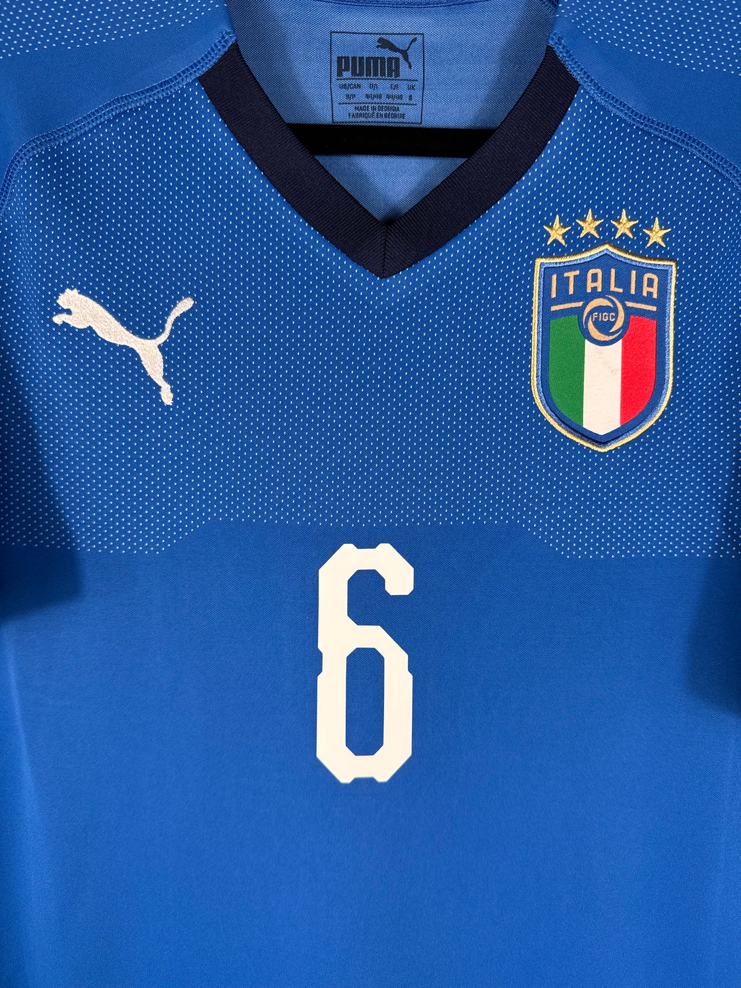 Gros plan sur l'écusson de la fédération italienne avec 4 étoiles et le logo Puma blanc sur fond bleu.
