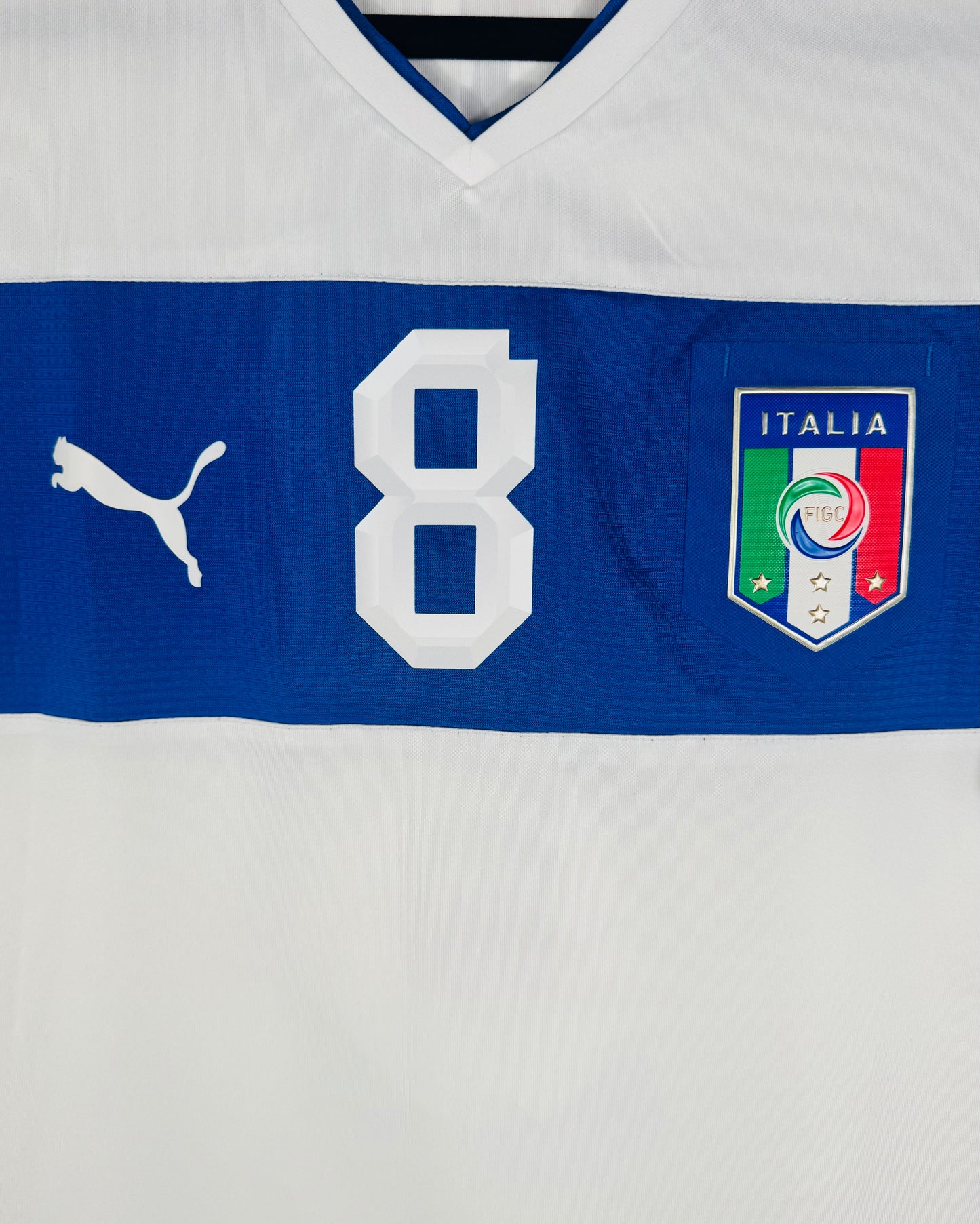 Gros plan sur l'écusson FIGC Italie et le numéro 8 centrés sur la bande bleue du maillot.