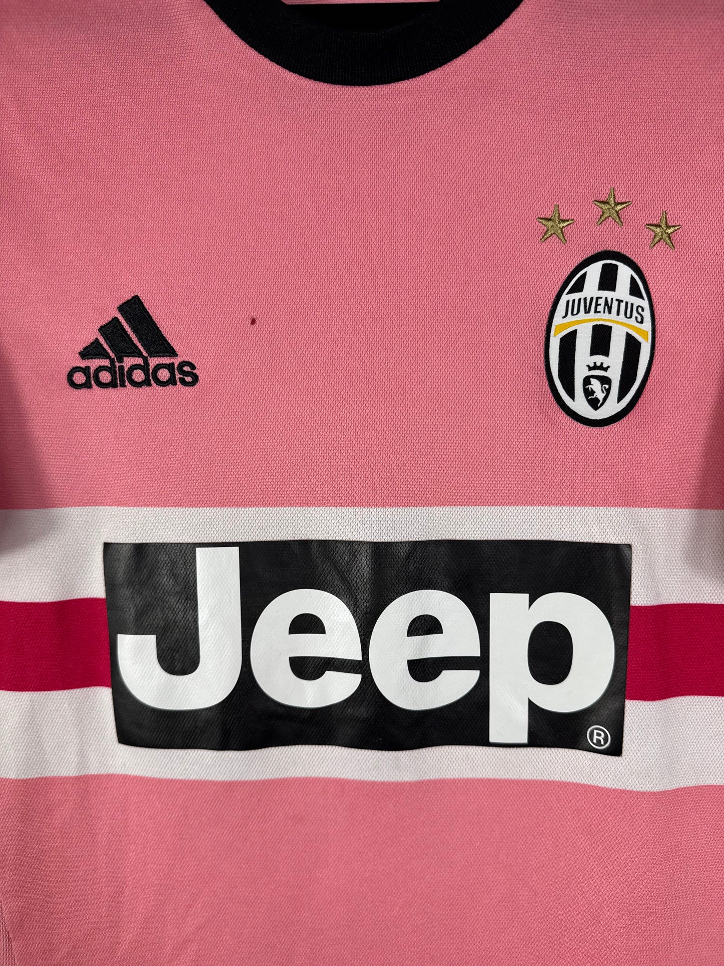 Gros plan sur l'écusson de la Juventus, le logo Adidas noir et le sponsor Jeep sur le maillot rose.