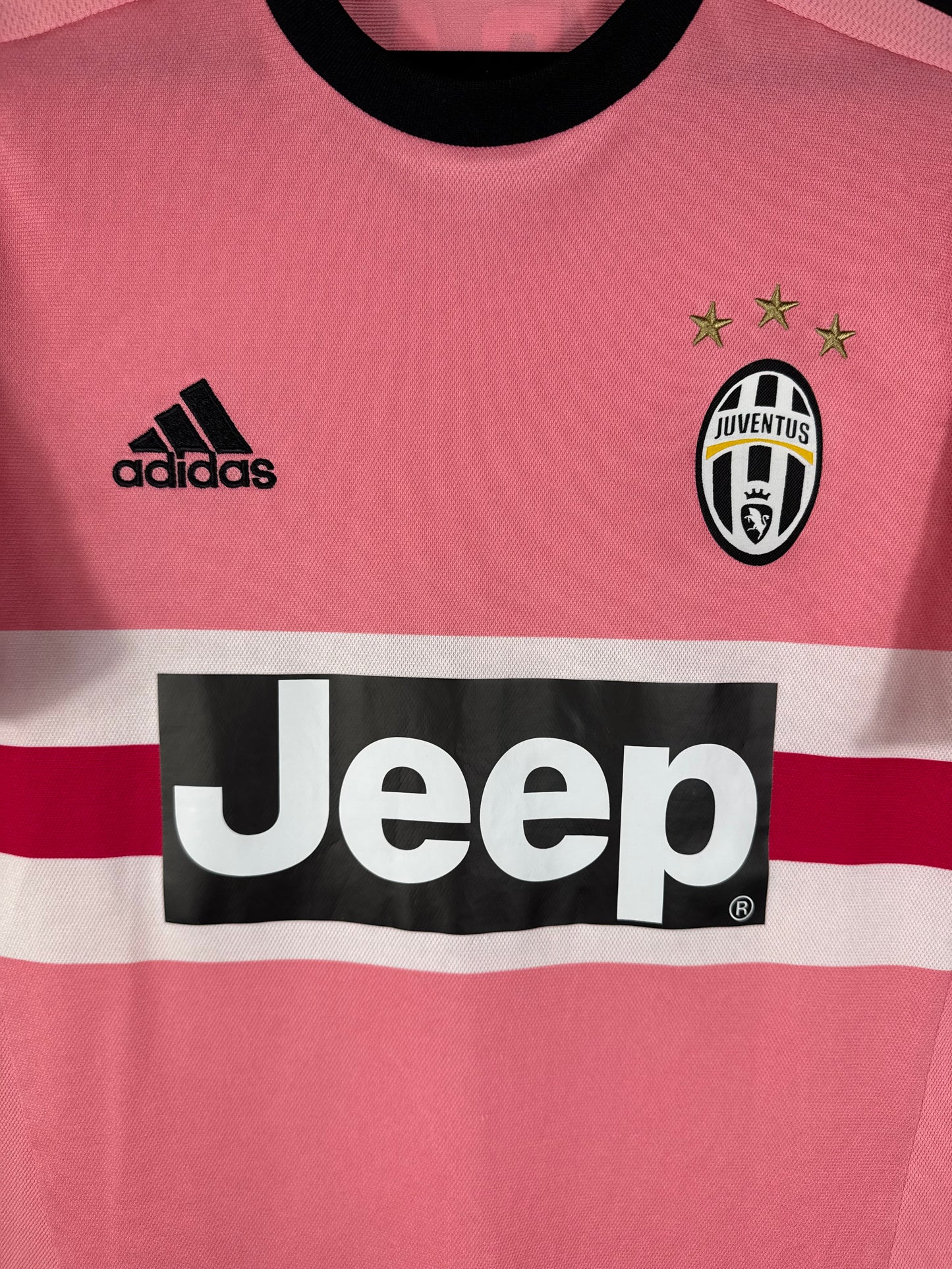 Gros plan sur l'écusson de la Juventus avec ses 3 étoiles d'or et le logo Adidas noir sur le maillot rose.