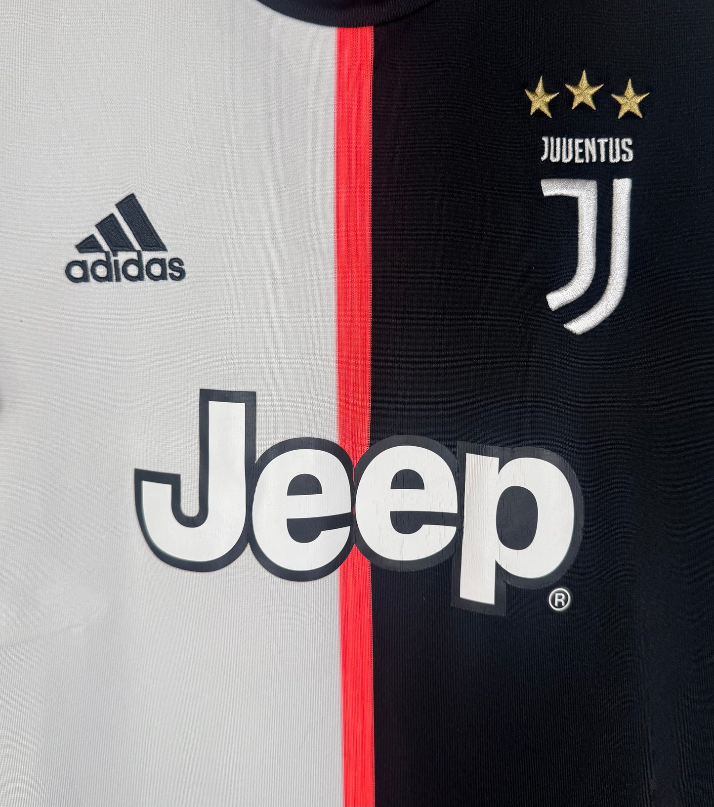 Gros plan sur le logo J de la Juventus, le logo Adidas et le sponsor Jeep sur fond bicolore.