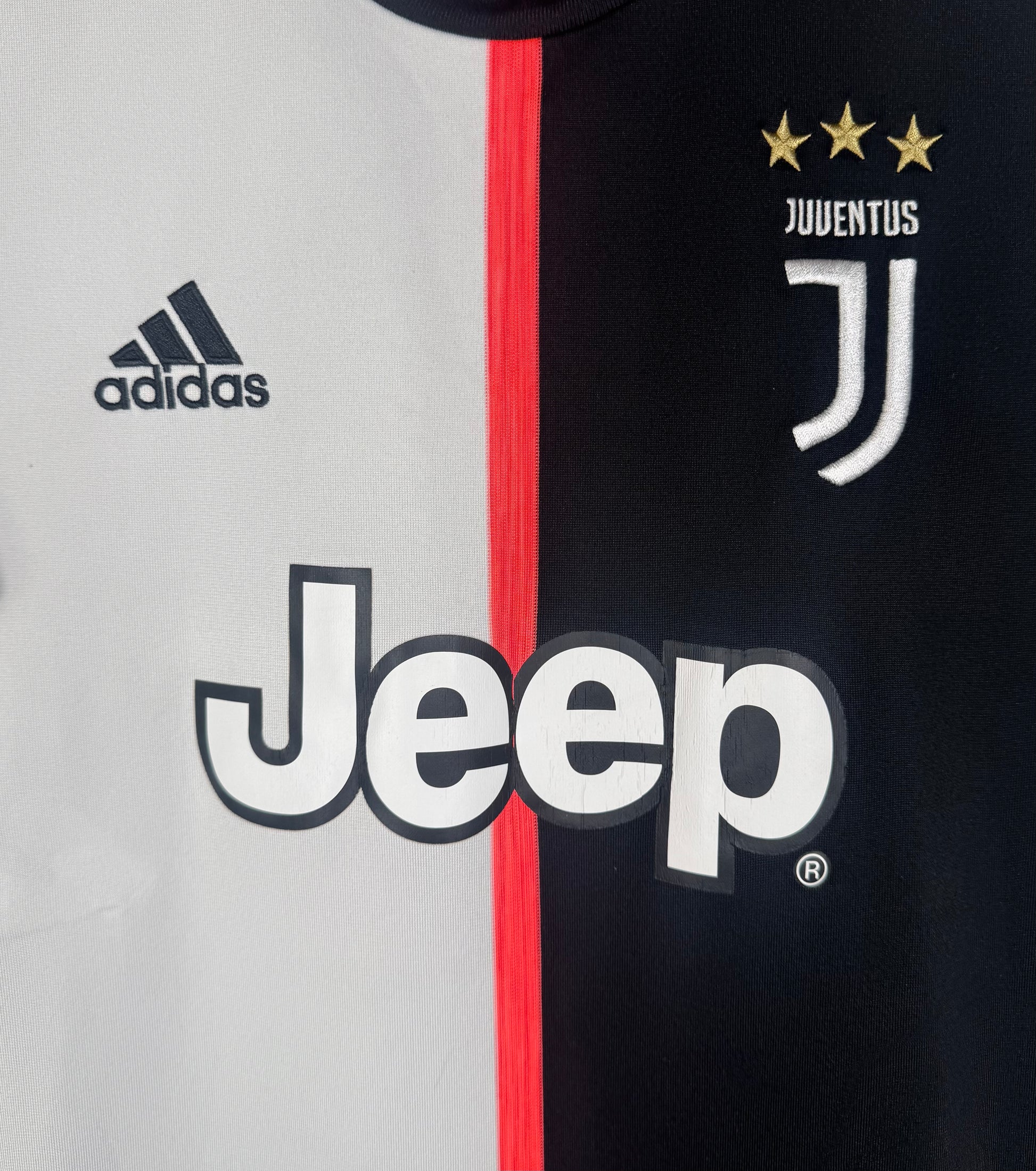 Gros plan sur le logo J de la Juventus, le logo Adidas et le sponsor Jeep sur fond bicolore.