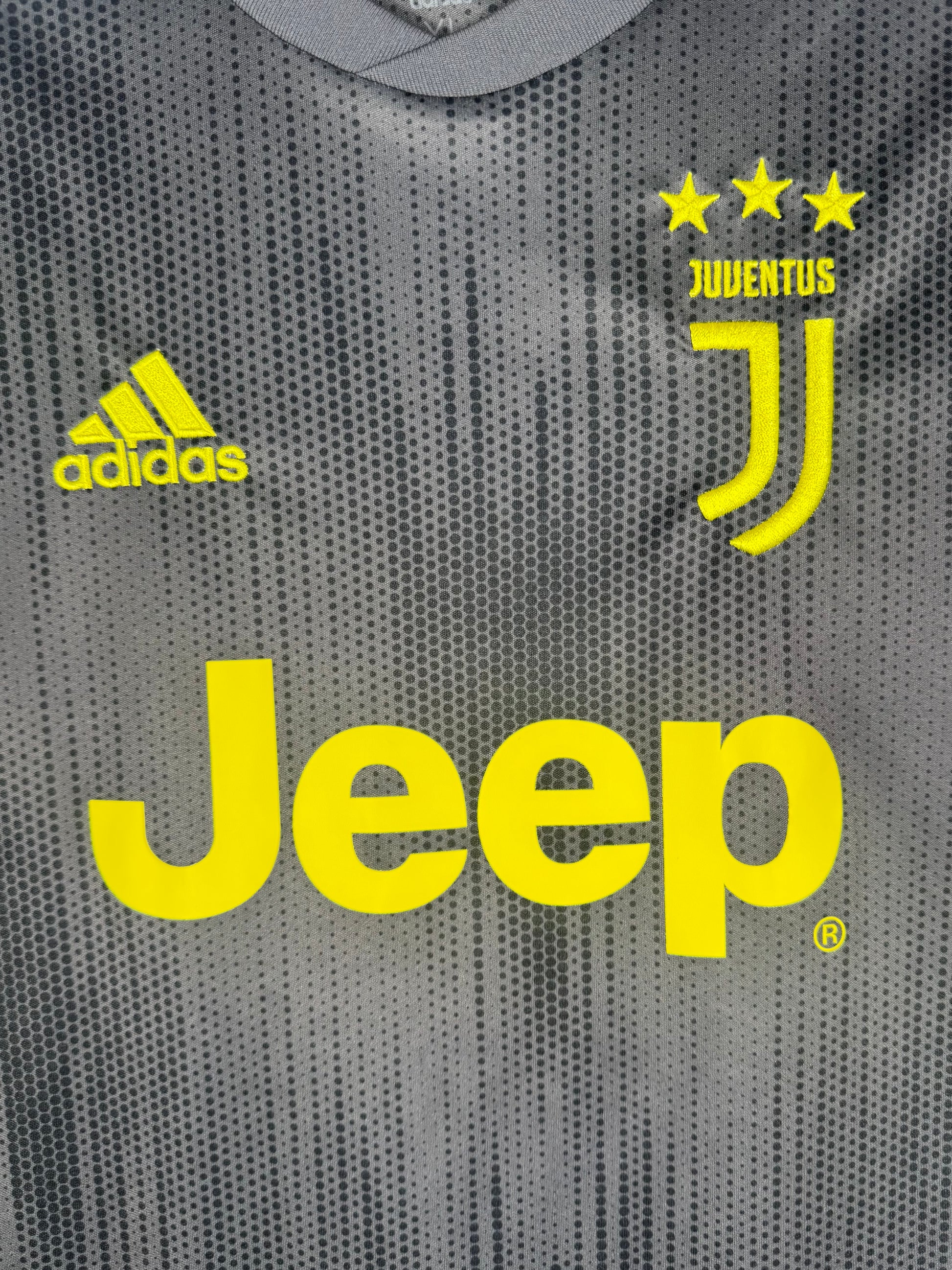 Gros plan sur le logo J de la Juventus et le sponsor Jeep en jaune fluo sur tissu gris.