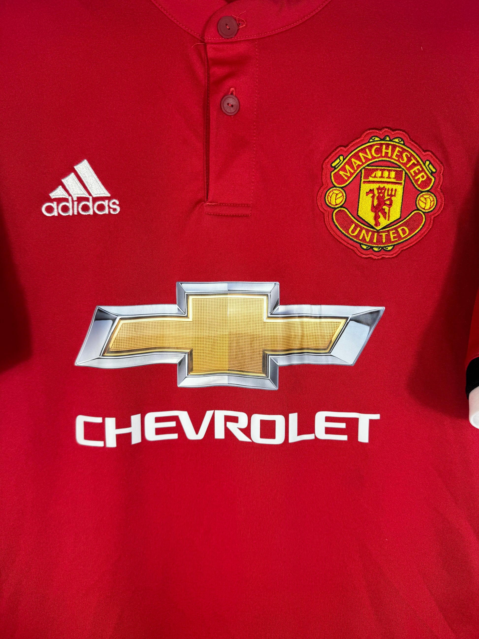 Gros plan sur l'écusson de Manchester United brodé et le détail du col à deux boutons.